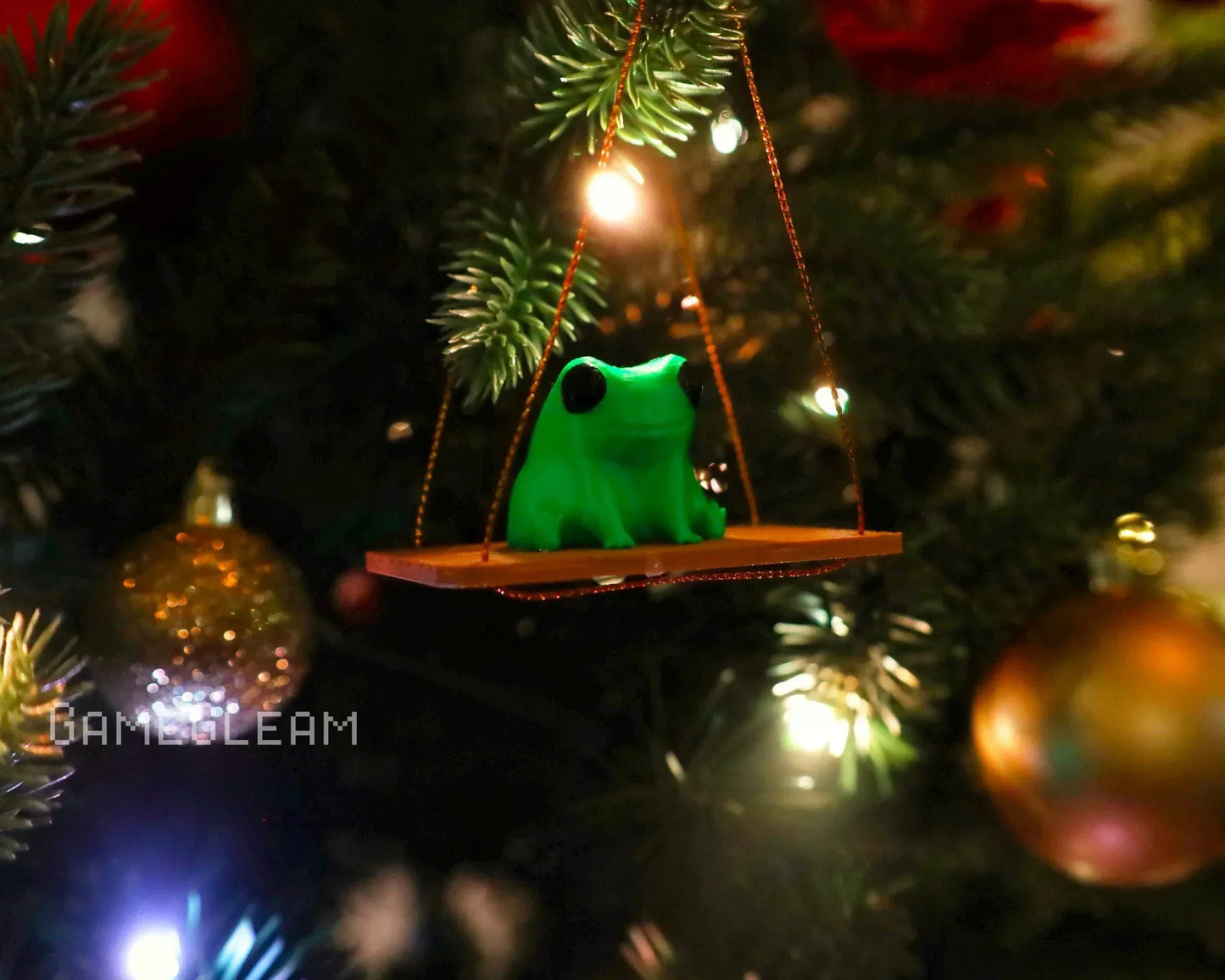 Green frog ornament on swing, hanging on Christmas tree with festive lights and baubles