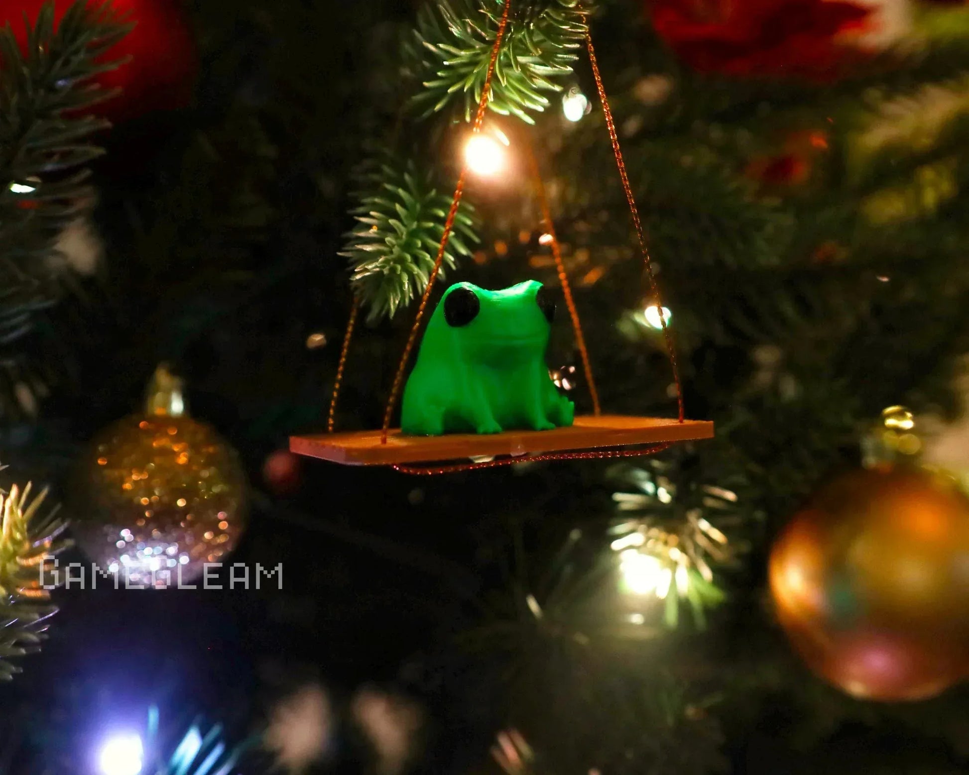 Green frog ornament on swing, hanging on Christmas tree with festive lights and baubles