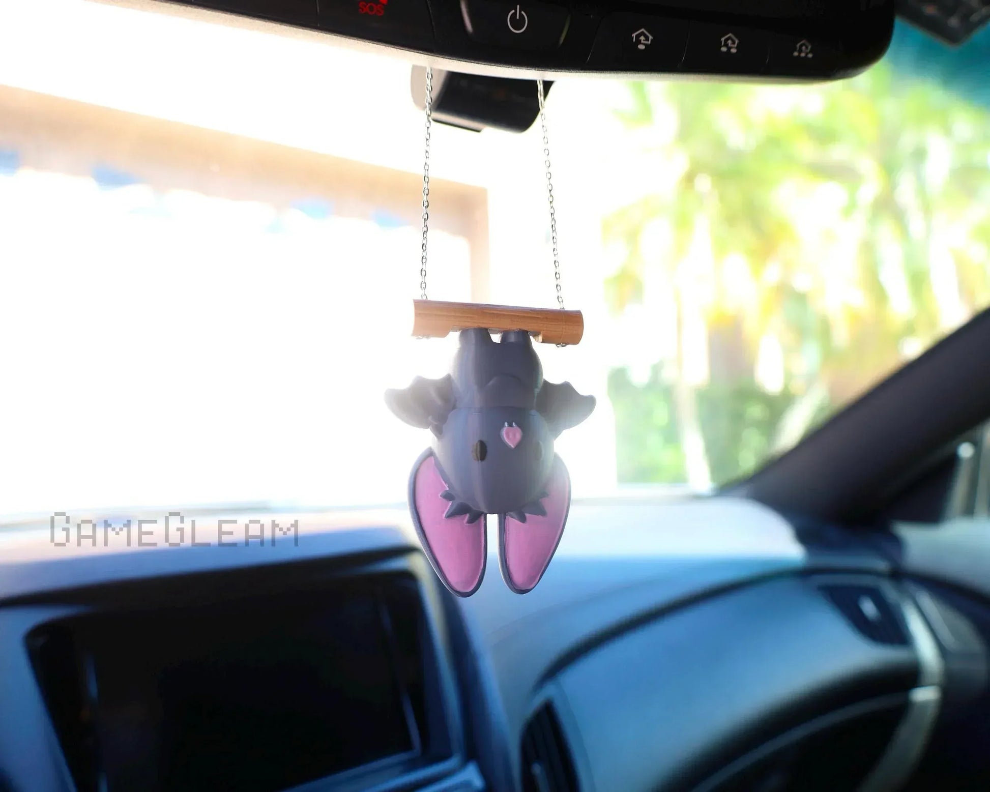Cute bat ornament with pink ears hanging from a car rearview mirror with a chain.