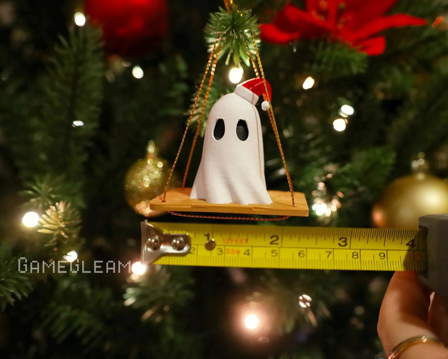 Handmade ghost ornament with Santa hat on swing, measured against tape, hanging on Christmas tree