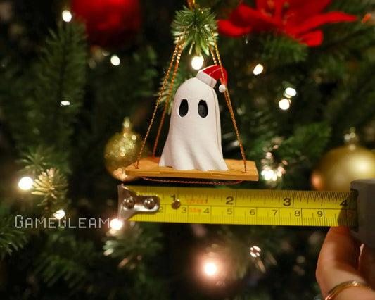 Handmade ghost ornament with Santa hat on swing, measured against tape, hanging on Christmas tree