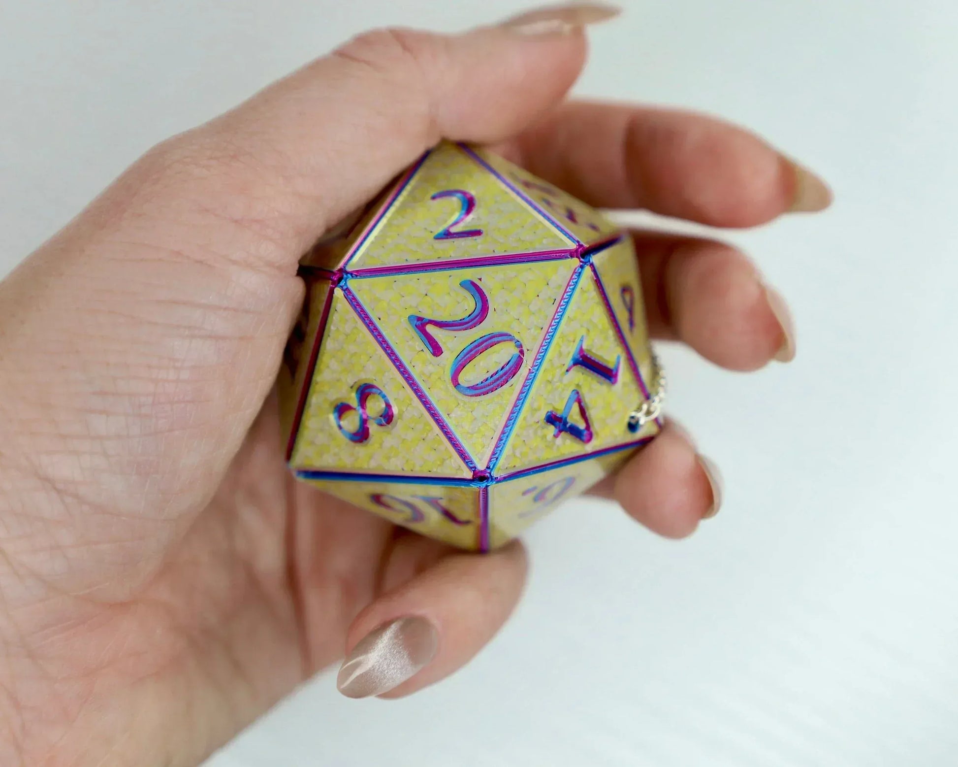 Hand holding a large holographic yellow 20-sided dice charm with purple numbers