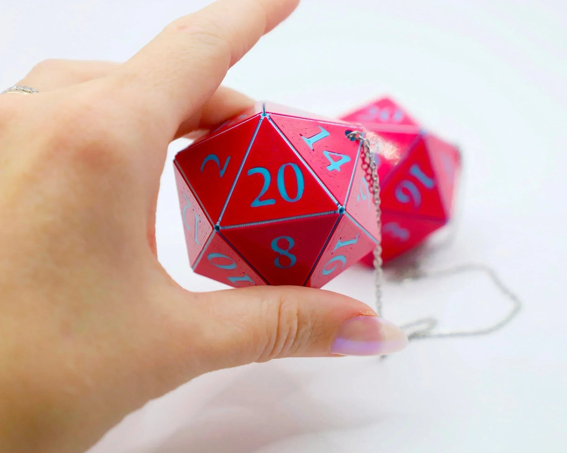 Hand holding a red 20-sided dice car charm with blue numbers and metal chain.