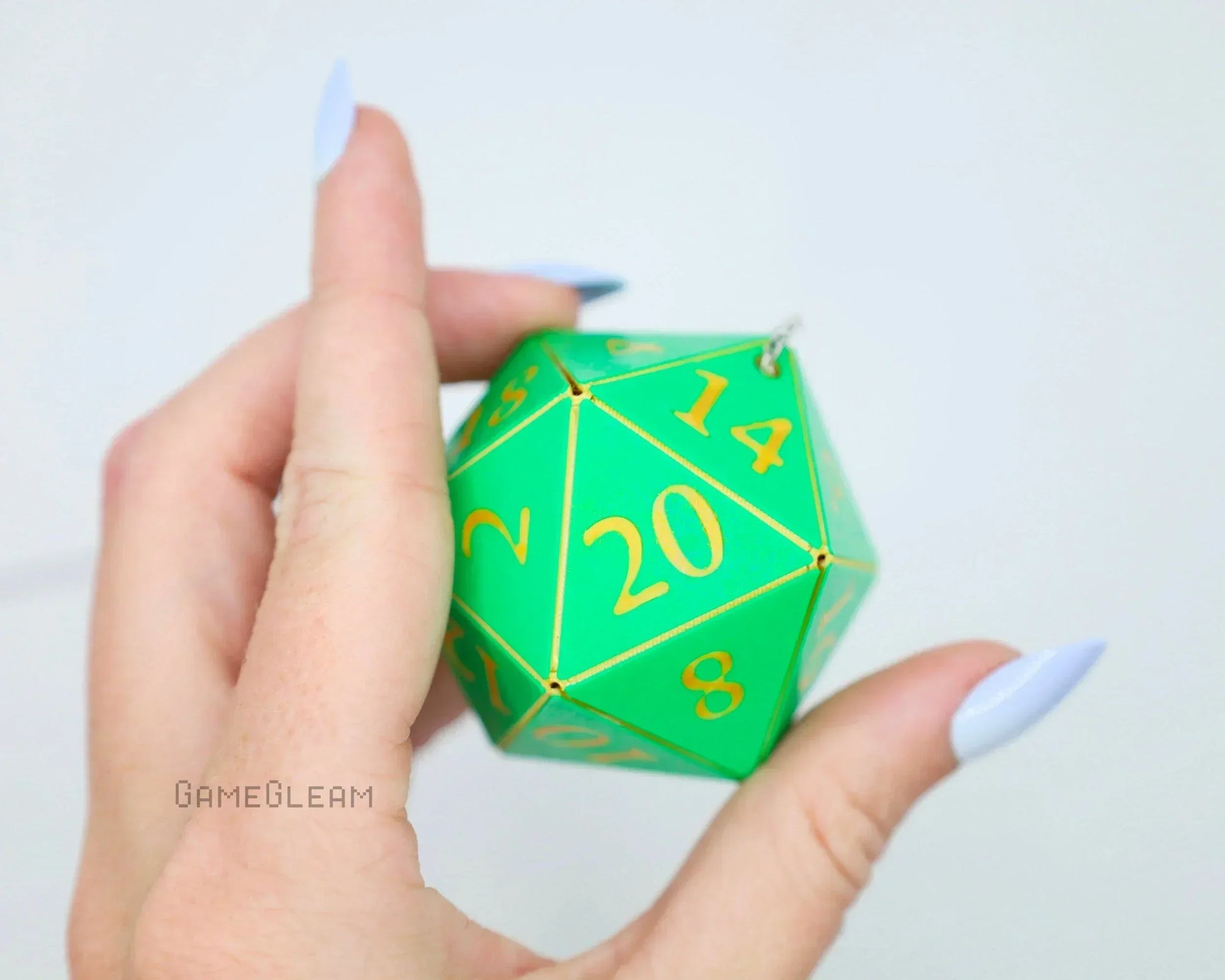 Hand holding a green twenty-sided dice car charm with gold numbers, gamer accessory