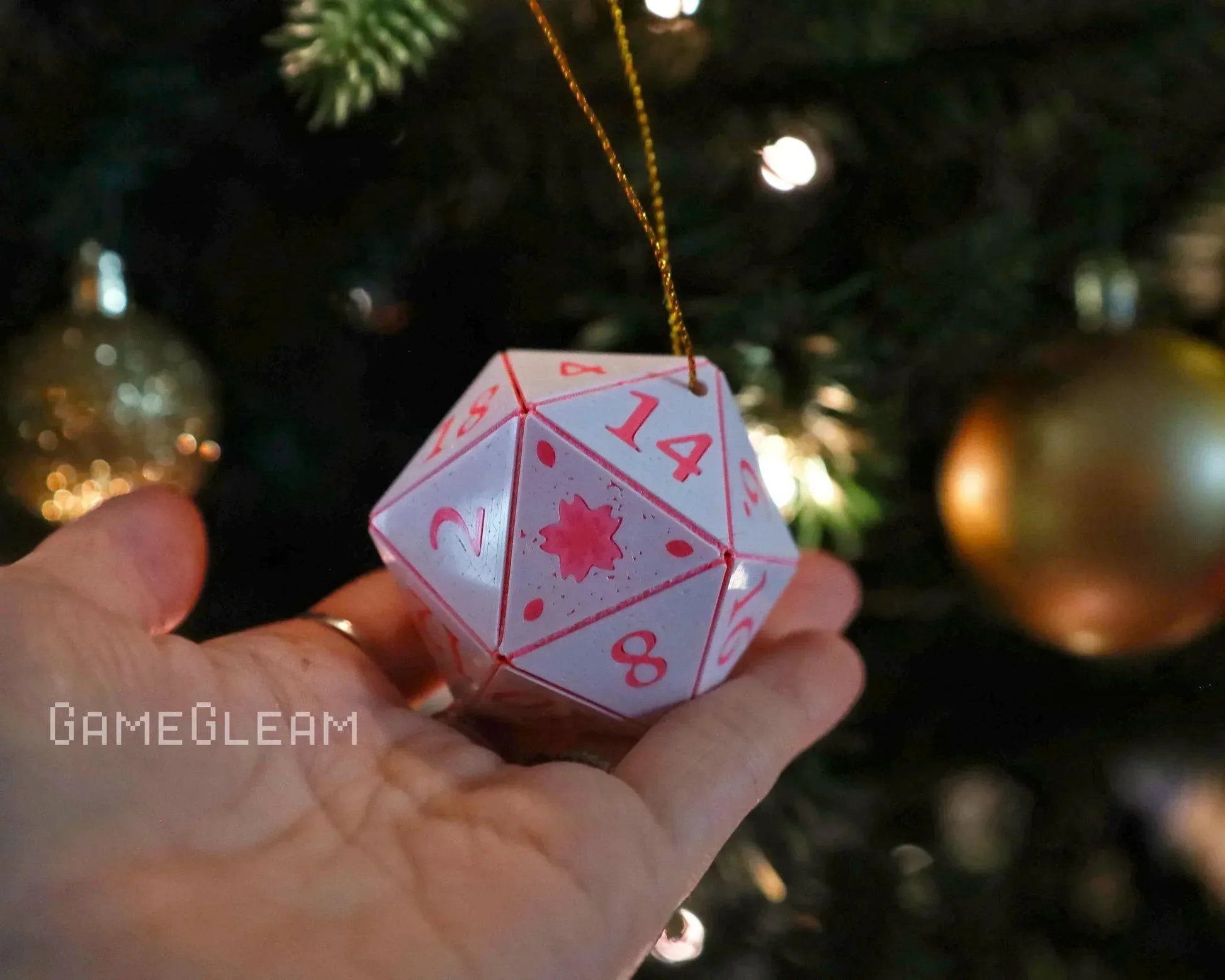 Hand holding pink and white 20-sided dice ornament by a decorated Christmas tree