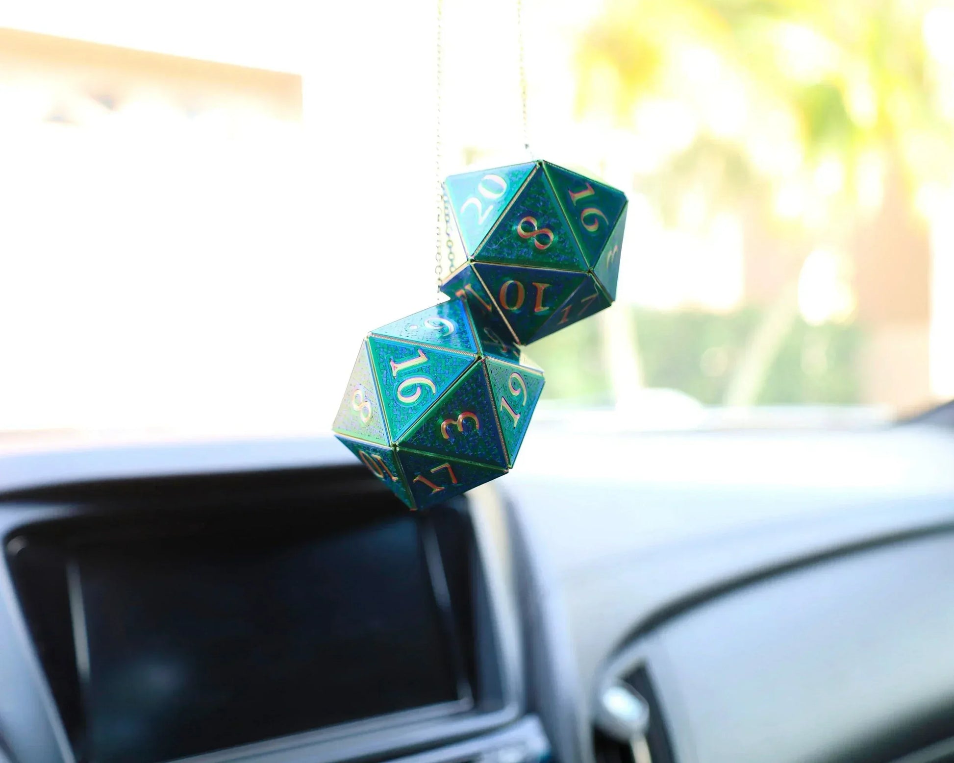 Holographic green twenty-sided dice car charm hanging from rearview mirror
