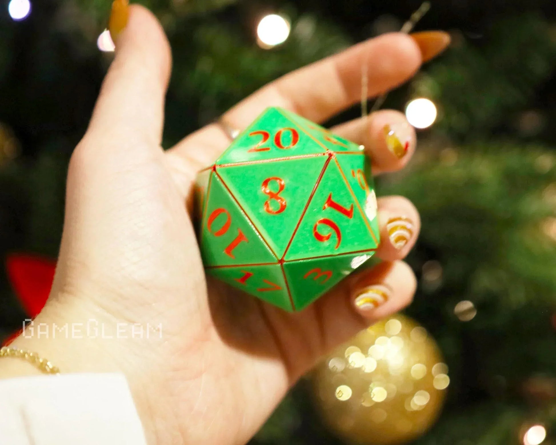 Hand holding a green twenty-sided dice charm with red numbers near a Christmas tree