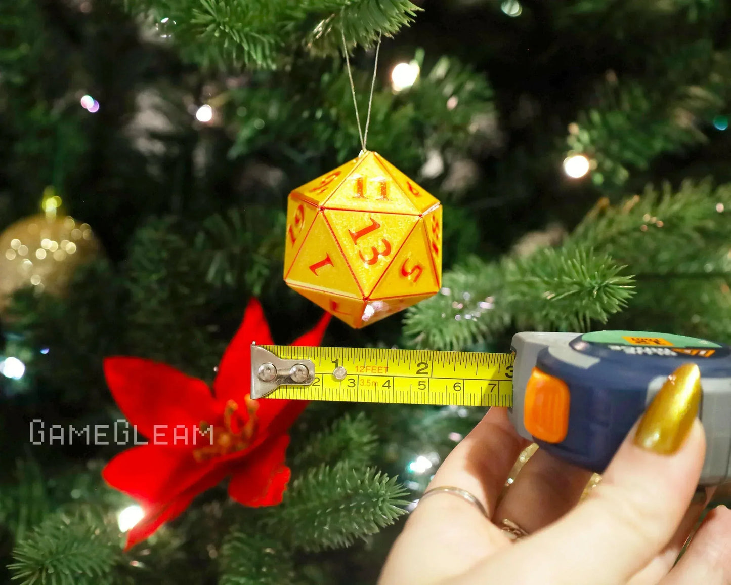 Yellow and red 20-sided dice ornament measured with tape on a Christmas tree.