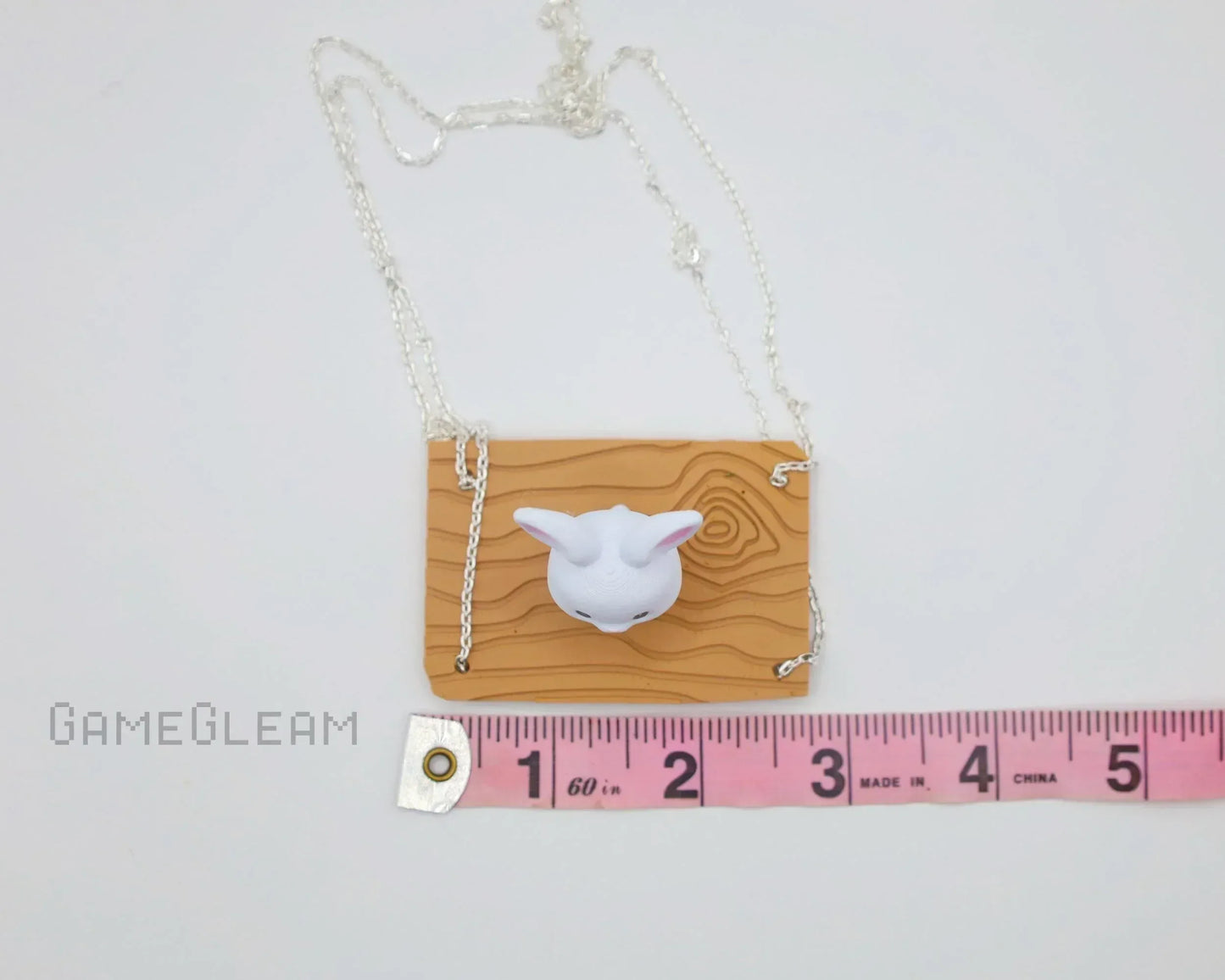 Handmade necklace with carved wood pattern plaque and white animal head charm, shown with measuring tape for scale.