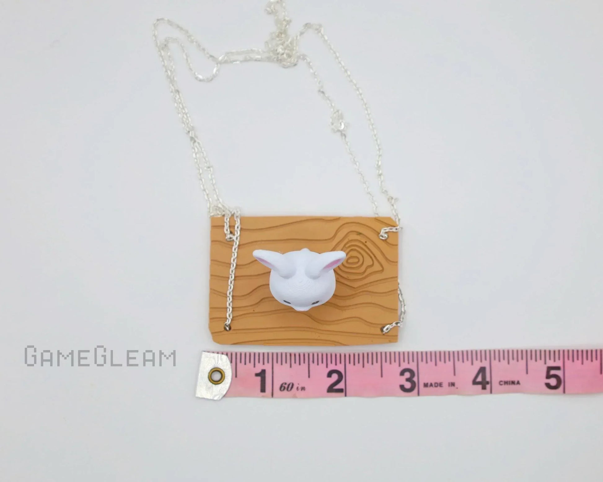 Handmade necklace with carved wood pattern plaque and white animal head charm, shown with measuring tape for scale.