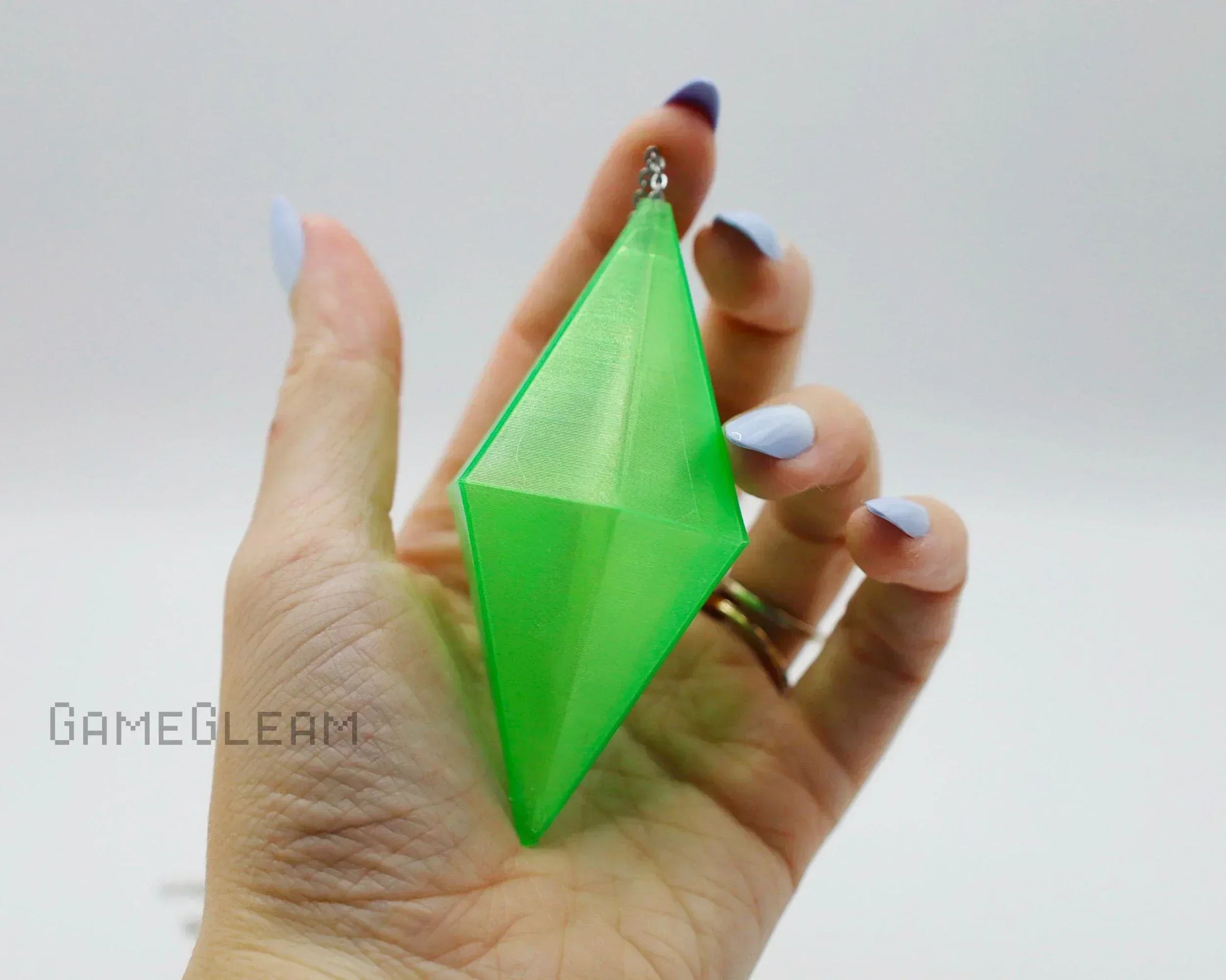 Hand holding a large green geometric prism-shaped gaming accessory charm