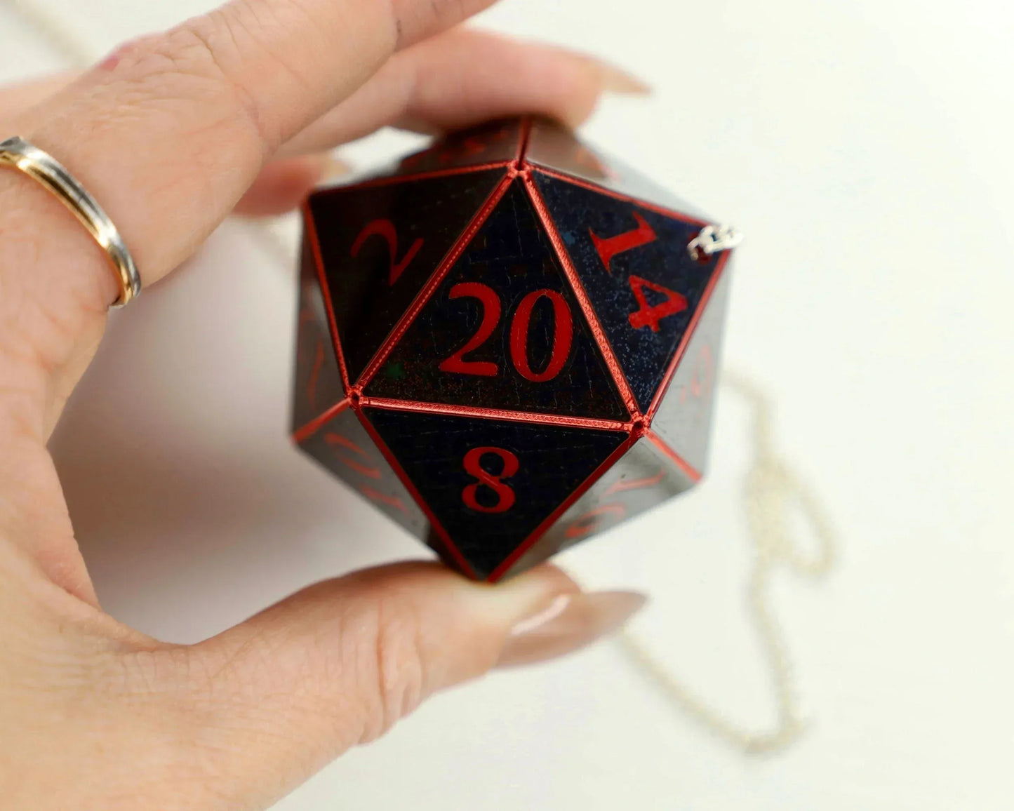 Hand holding large black twenty-sided RPG dice with red numbers and metal chain.