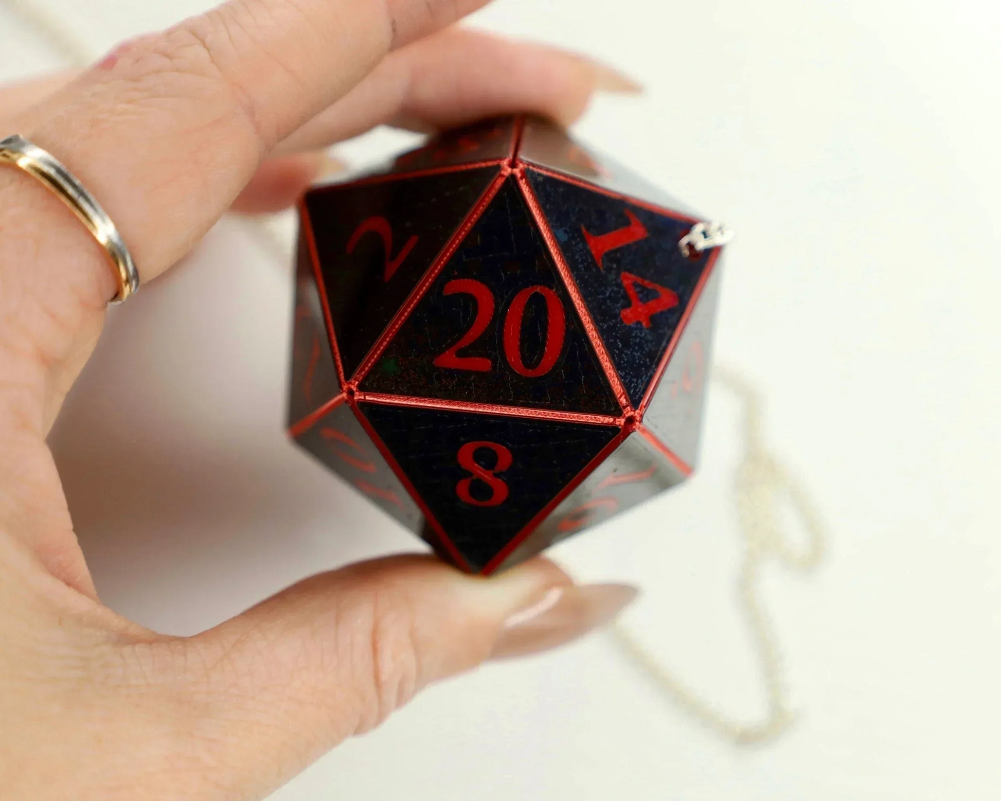 Hand holding large black twenty-sided RPG dice with red numbers and metal chain.