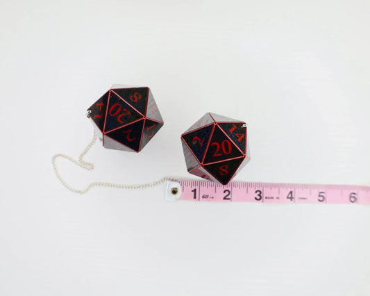 Two large black and red twenty-sided dice car charms with chain, next to a pink measuring tape