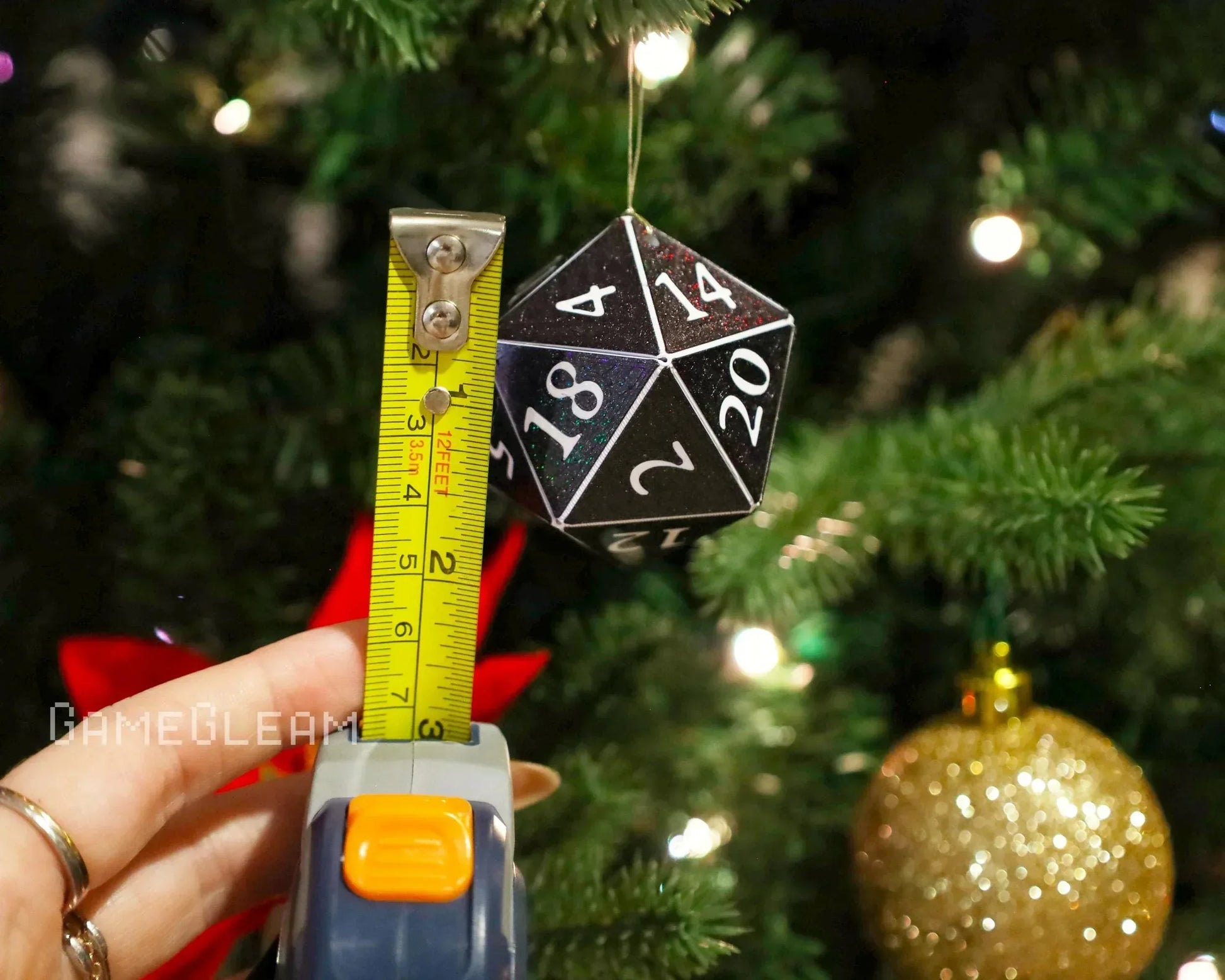 Black 20-sided dice ornament measured with tape, hanging on a Christmas tree