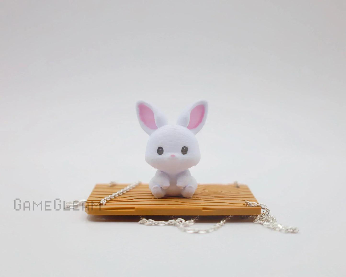 Cute white bunny figurine with pink ears on miniature wooden swing with silver chain