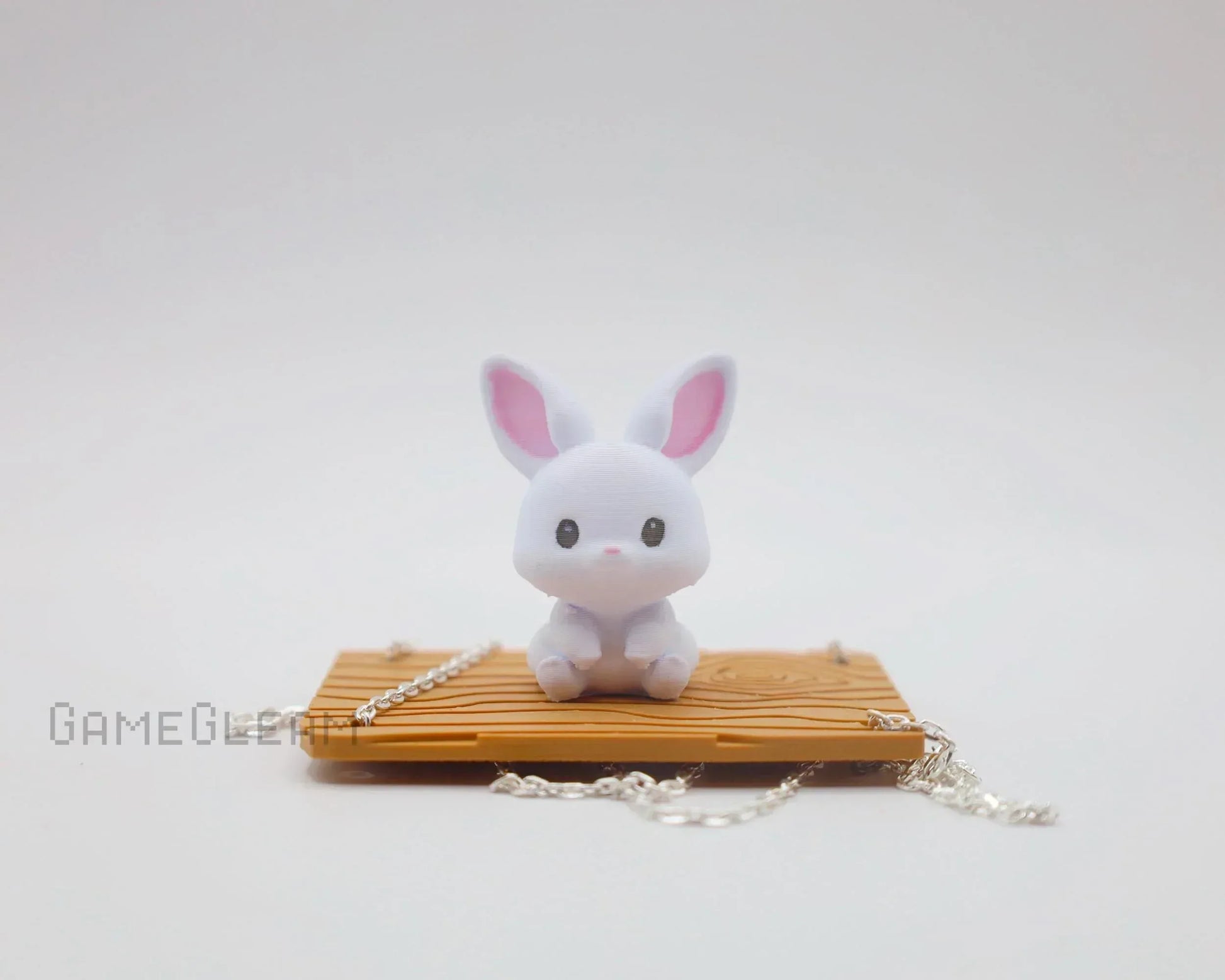 Cute white bunny figurine with pink ears on miniature wooden swing with silver chain