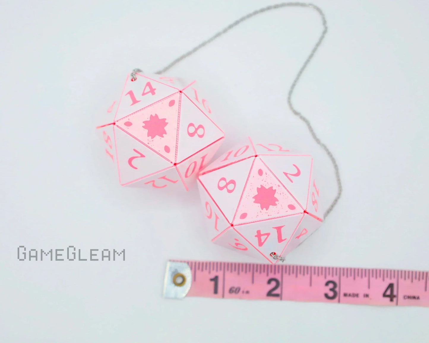Pair of pink and white twenty-sided car dice charms with measuring tape, perfect for gamer gifts