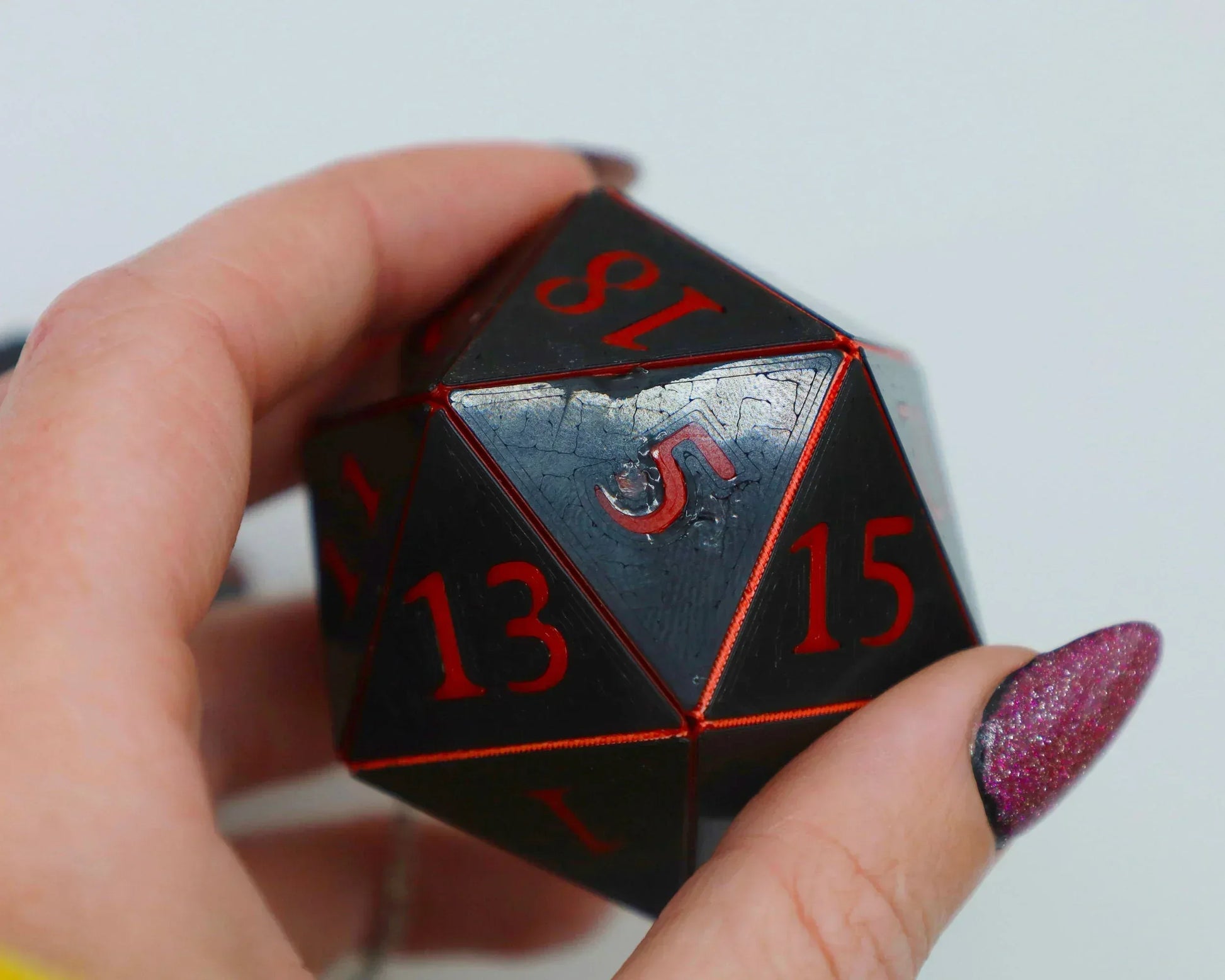 Hand holding a black 20-sided dice with red numbers, ideal for tabletop RPG gaming gifts
