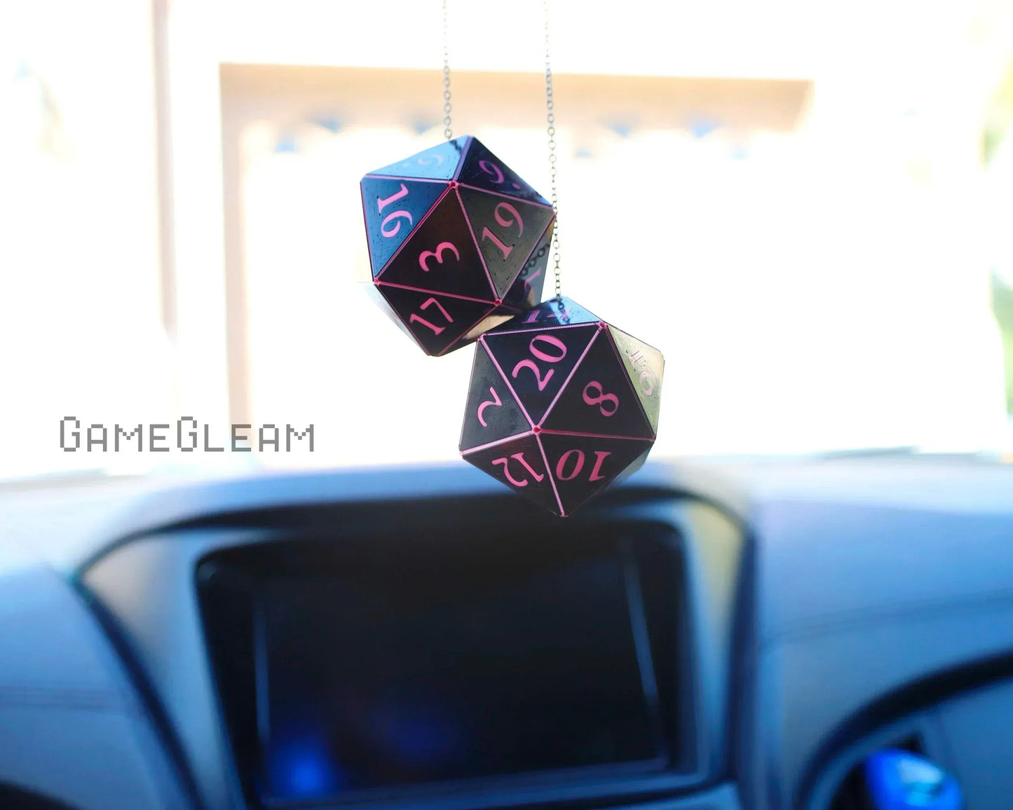Pink and black twenty-sided dice car charm hanging from rearview mirror in a car interior.