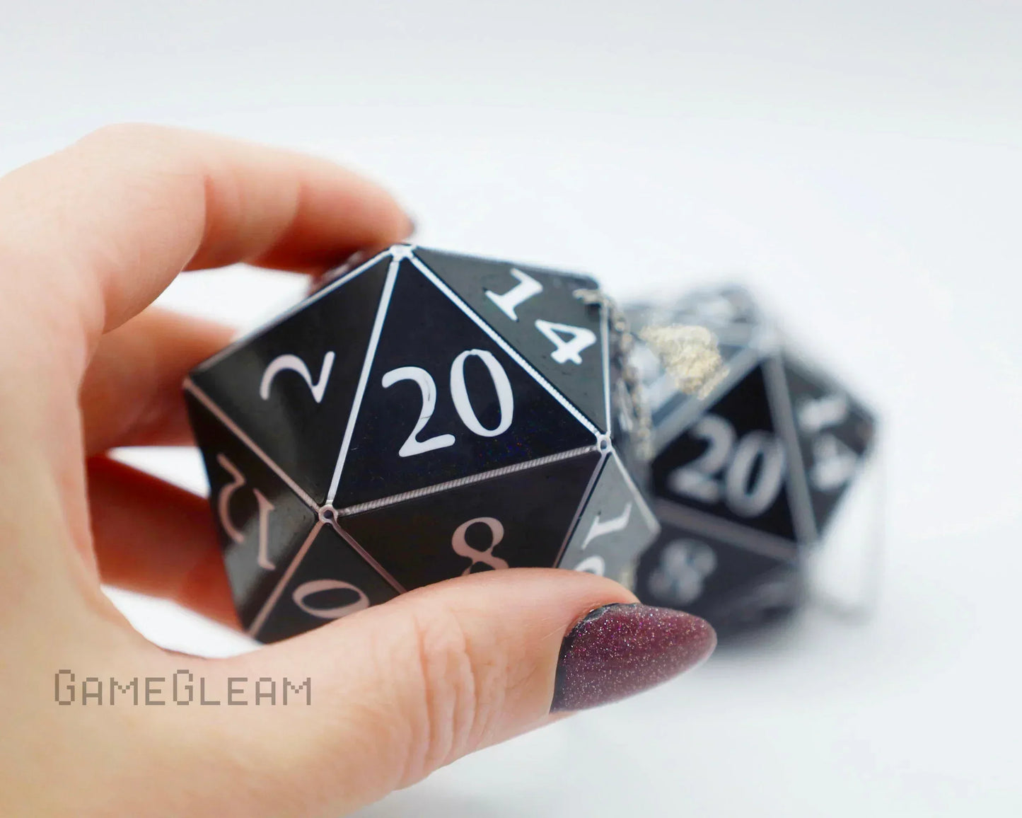 Hand holding a large black 20-sided polyhedral dice charm with white numbers for car or decor