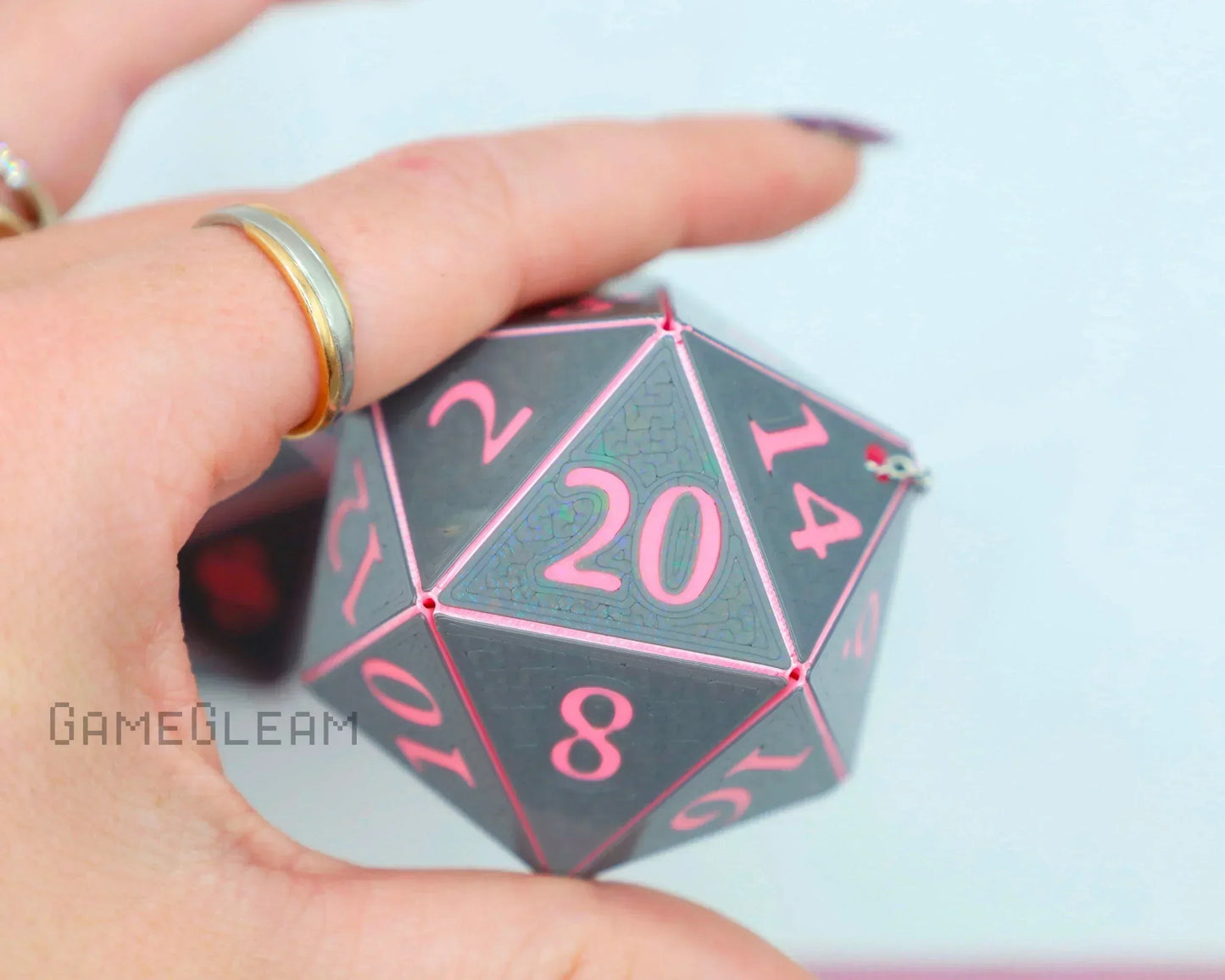Hand holding large gray and pink twenty-sided gamer dice charm accessory