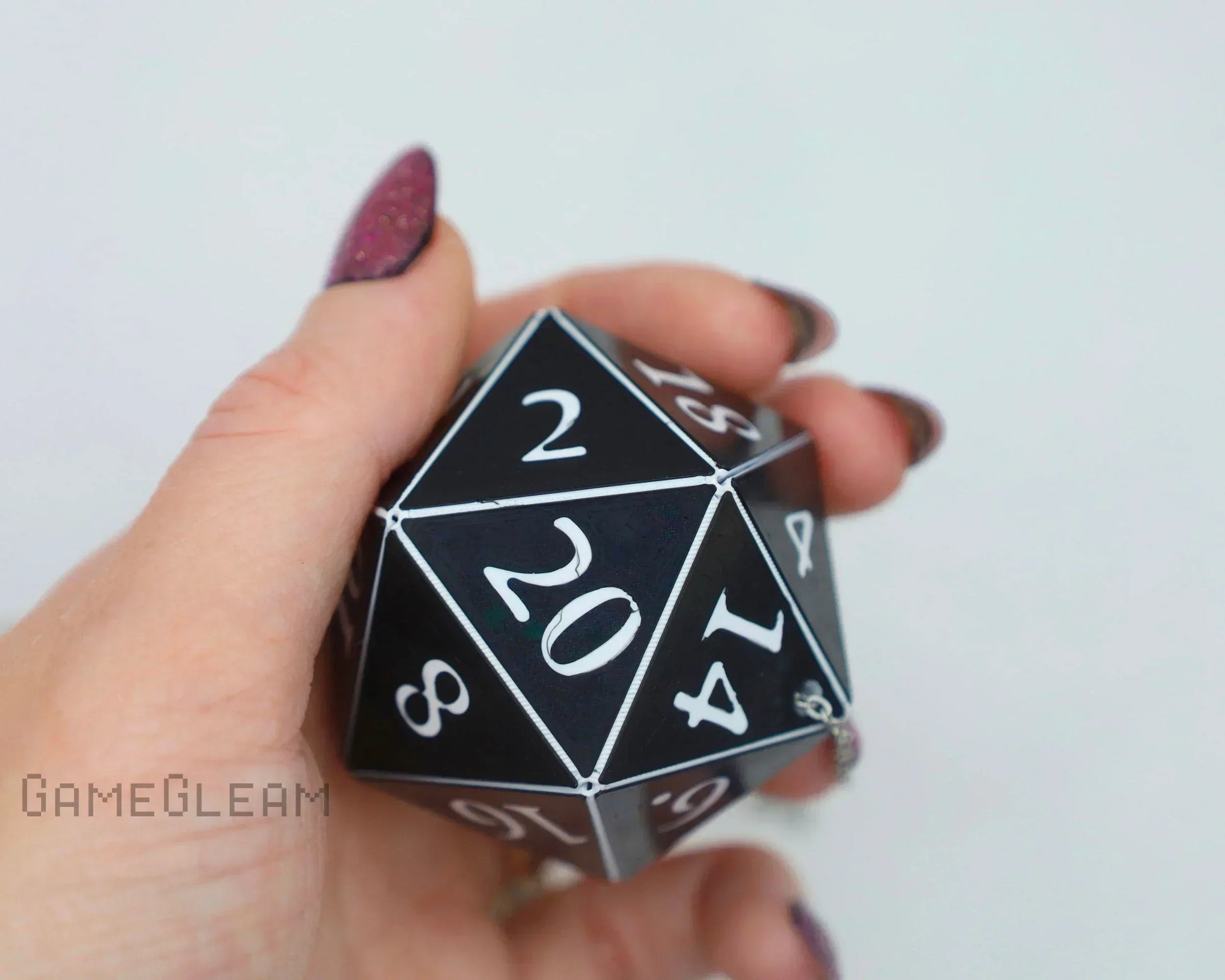 Hand holding black 20-sided polyhedral dice charm with white numbers, gamer accessory