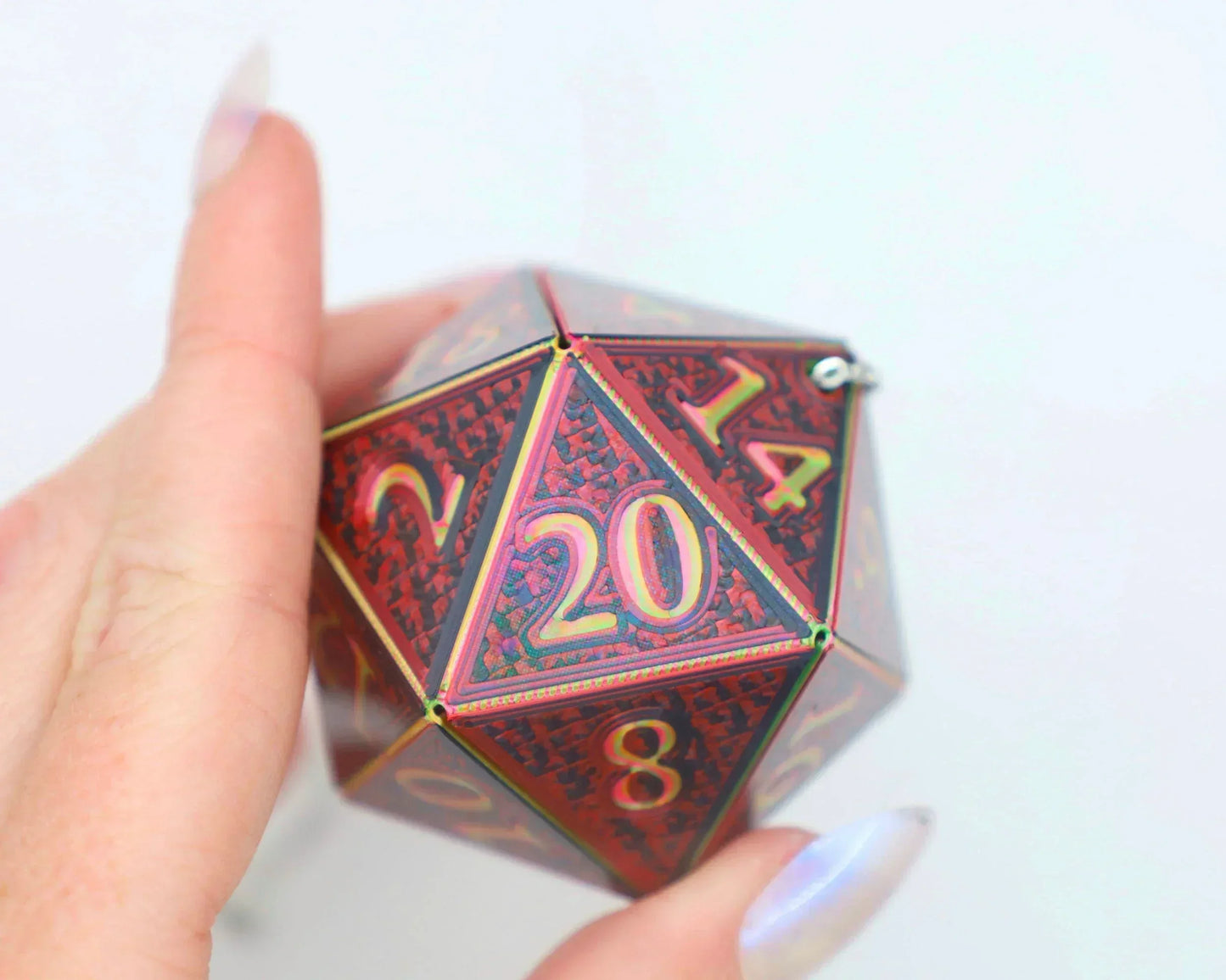 Hand holding a large red holographic 20-sided dice charm with gold numbers, gamer accessory