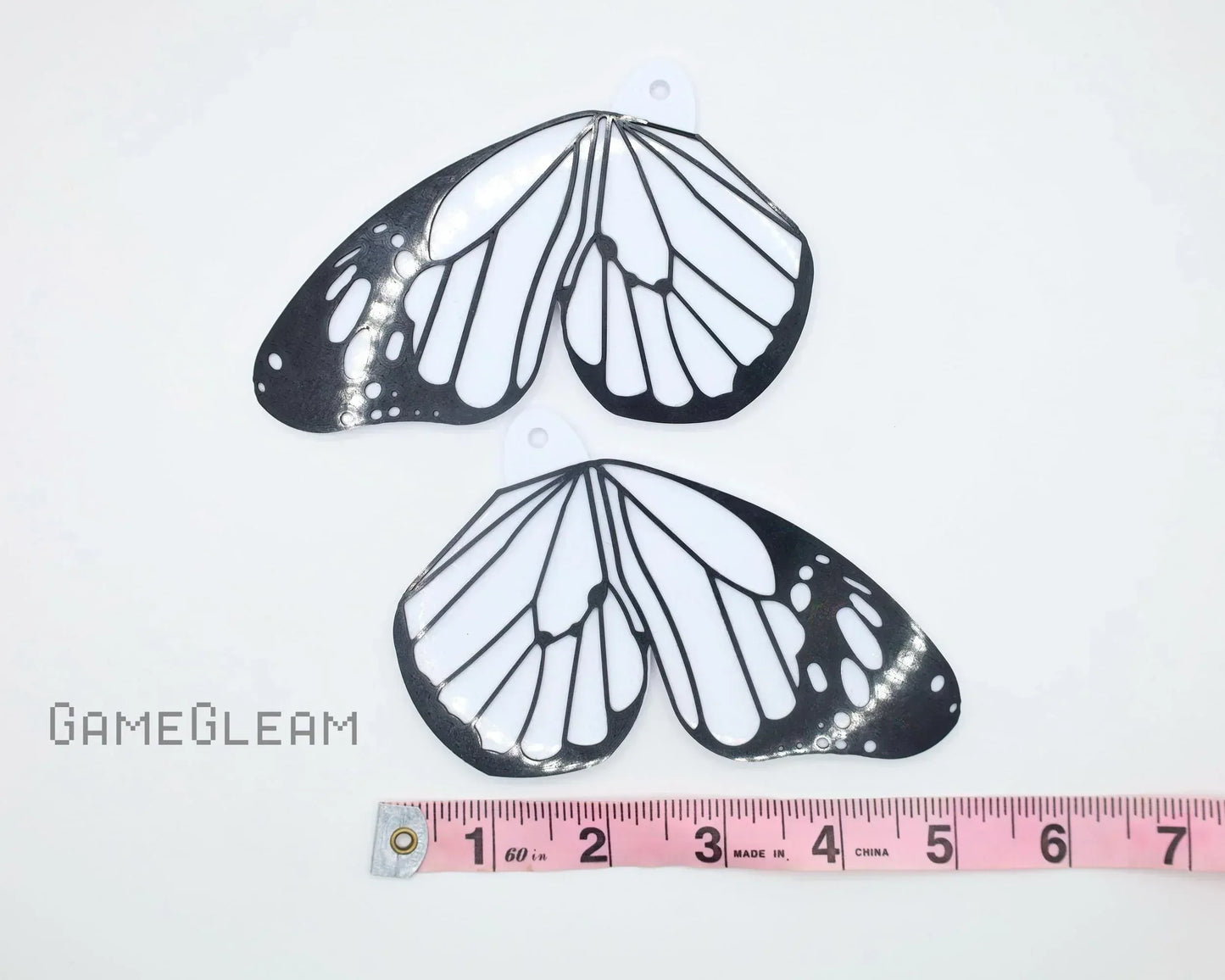 Pair of black and white butterfly wing car charms with a pink measuring tape