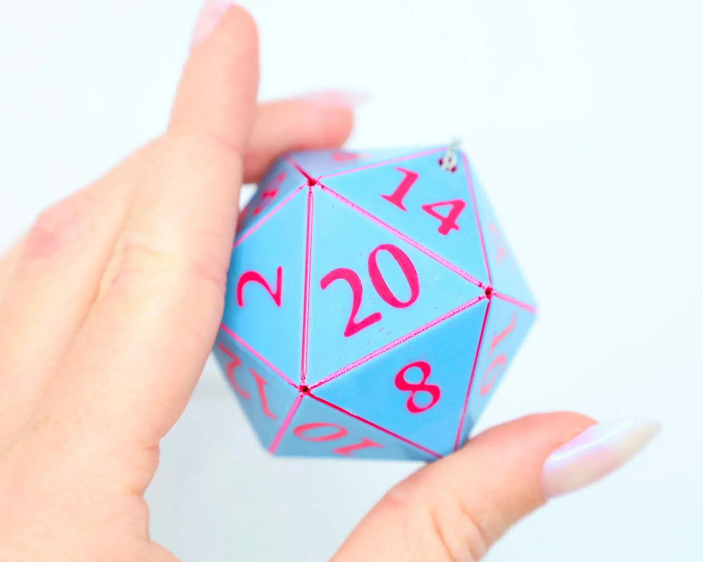 Hand holding a large blue twenty-sided dice car charm with pink numbers, close-up view