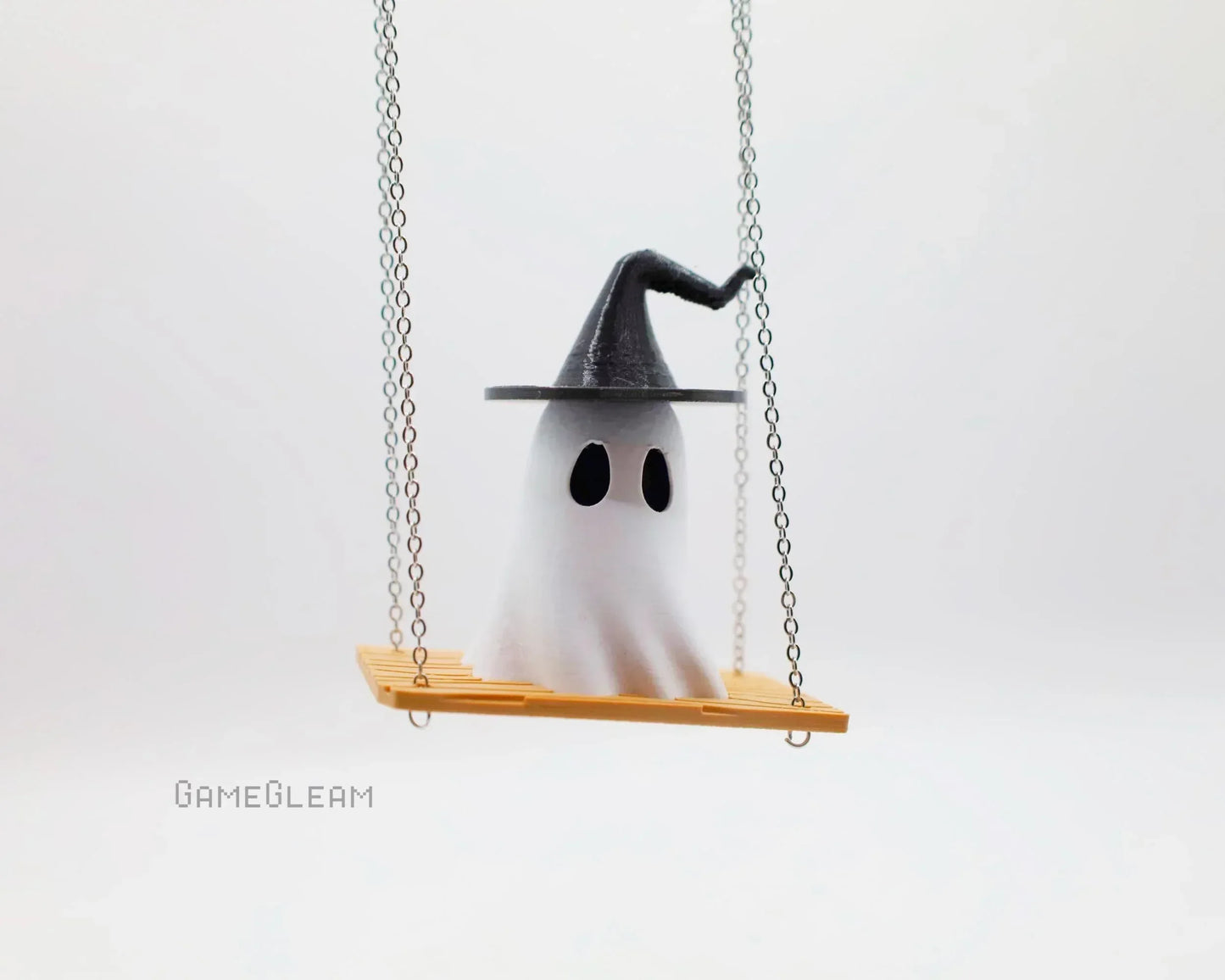 Cute ghost figurine with a wizard hat sitting on a wooden swing, white background.
