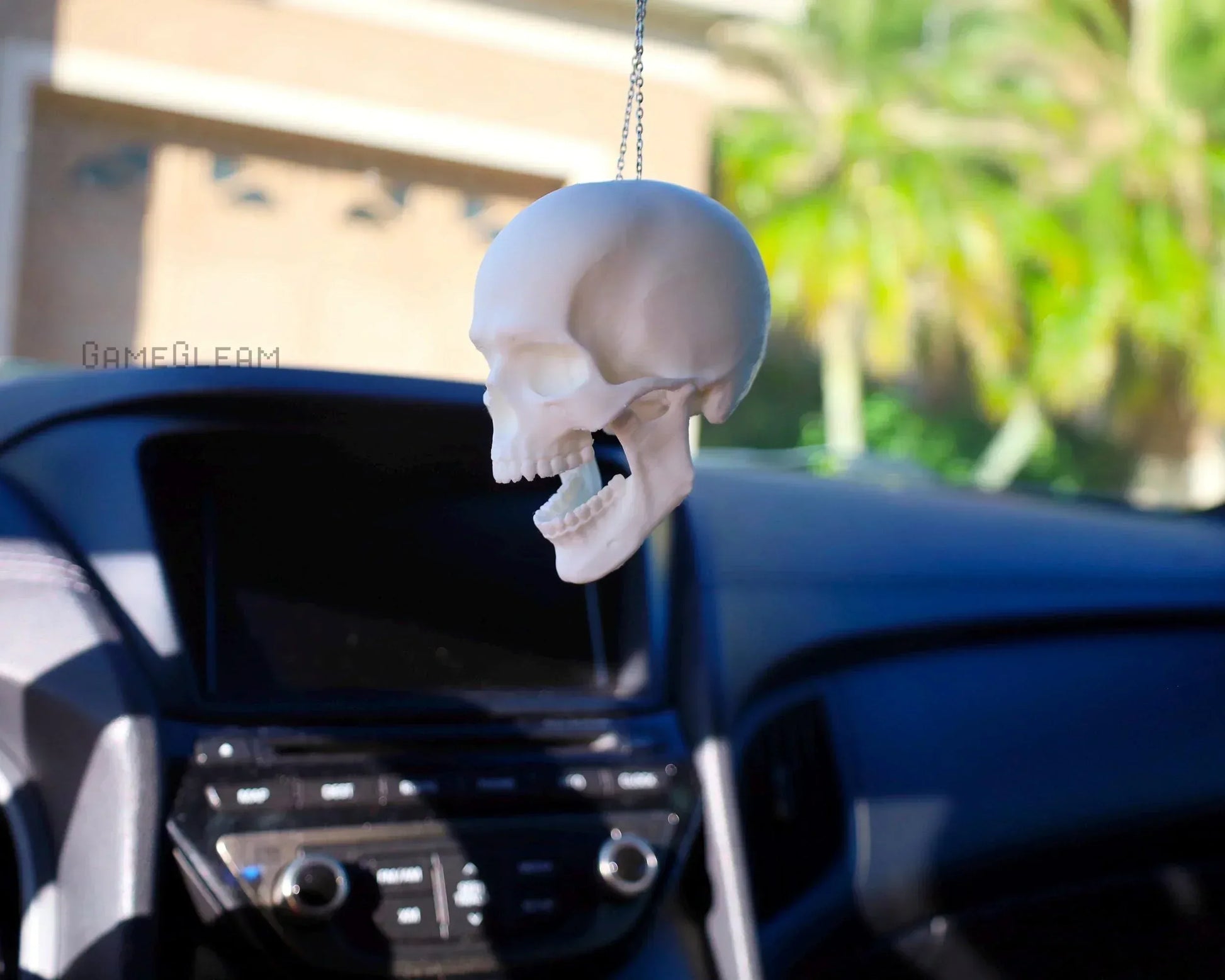 Handmade white skull car charm hanging from rearview mirror in sunny vehicle interior