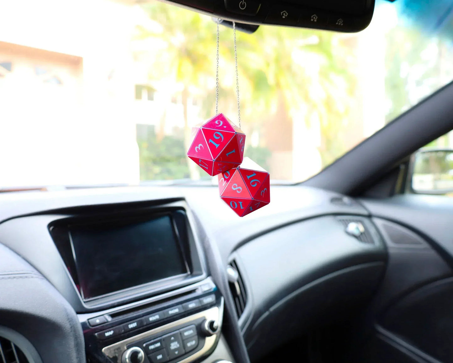 Red twenty-sided dice car charm hanging from rearview mirror in a car interior