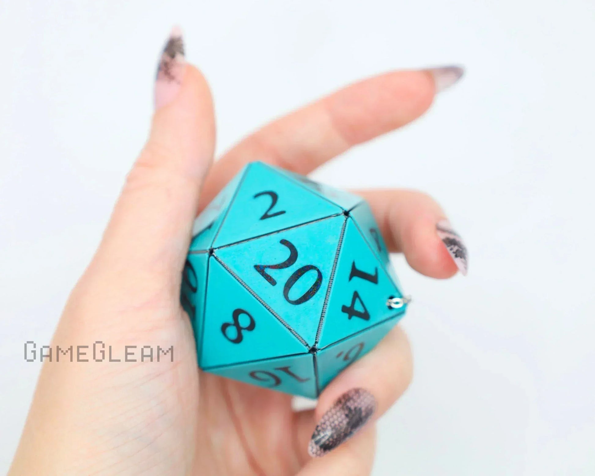 Hand holding large turquoise twenty-sided dice charm with bold black numbers