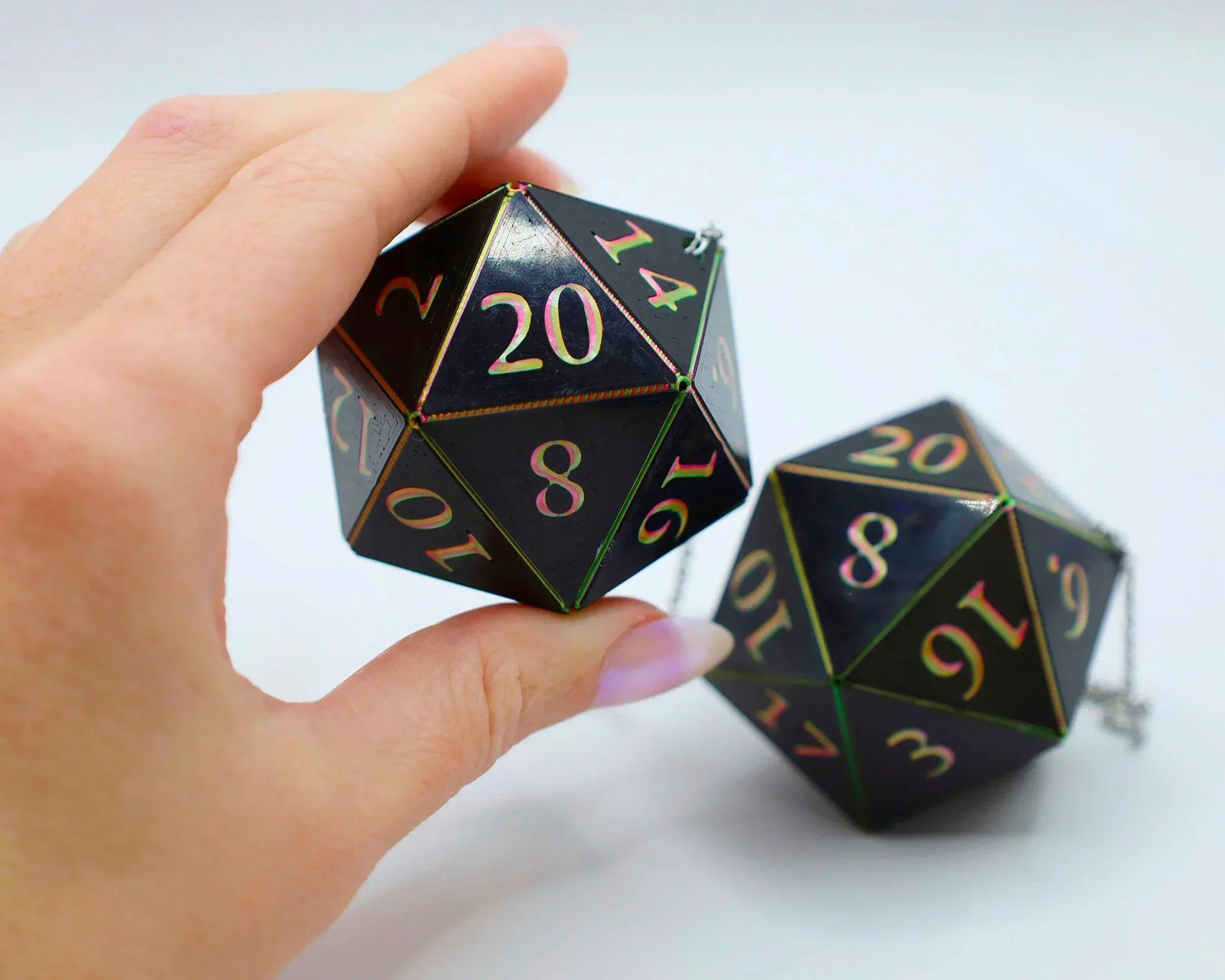 Hand holding black holographic 20-sided dice with colorful numbers, gamer car accessory