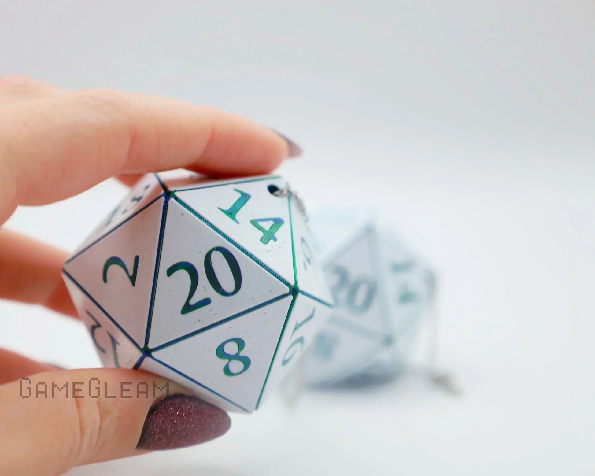Hand holding large white 20-sided dice charm with teal numbers, car accessory for gamers
