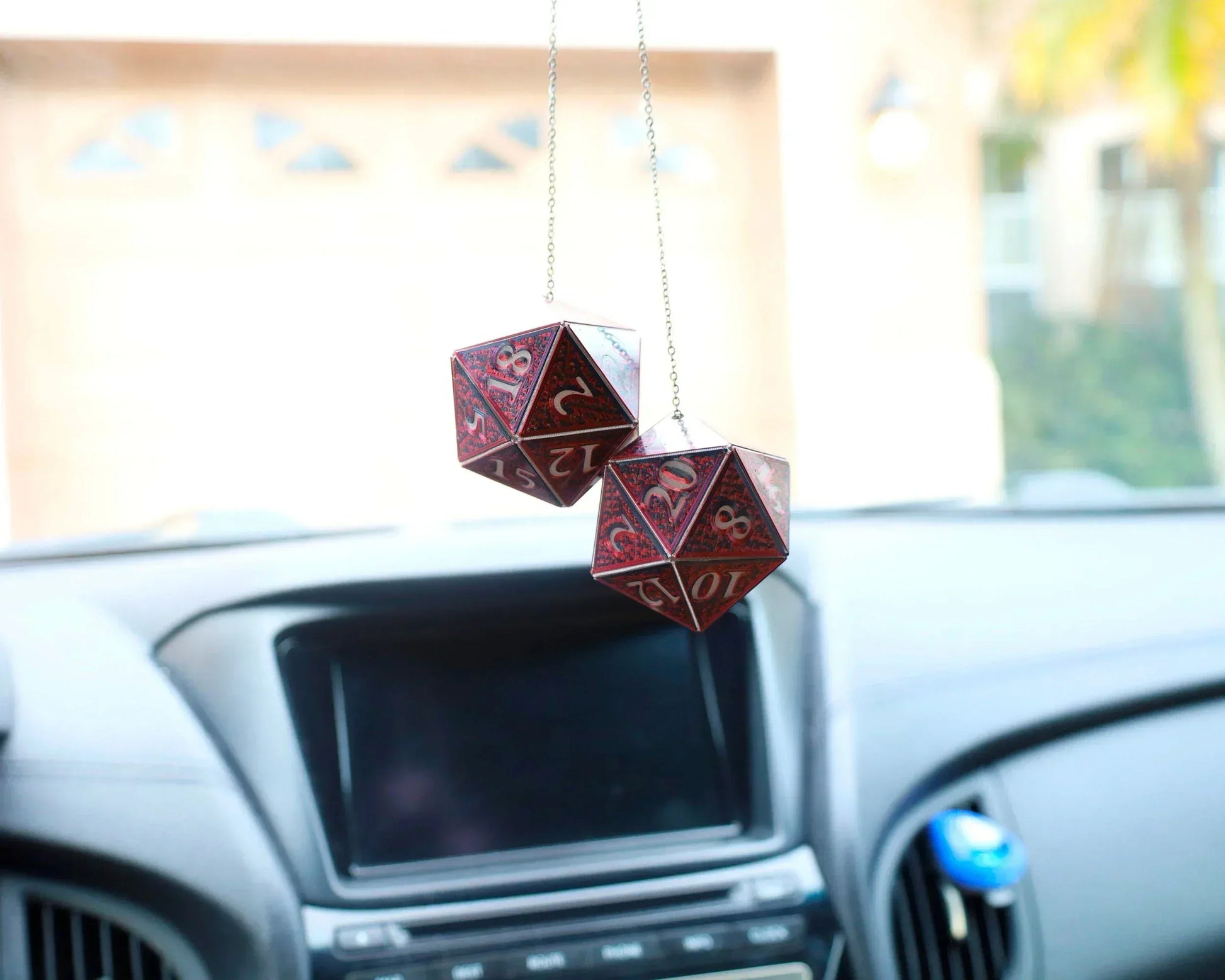 Holographic red and gold D20 dice car charm hanging from rearview mirror in modern car interior