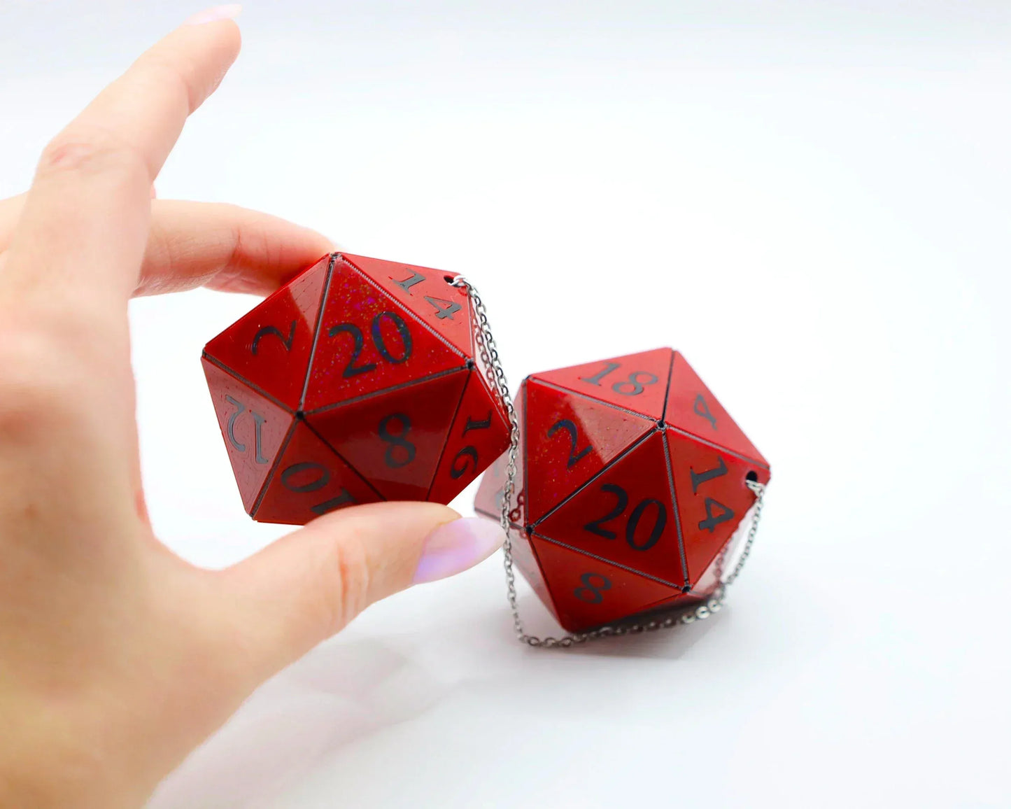 Hand holding two large red 20-sided dice with chains, tabletop gaming car accessory.
