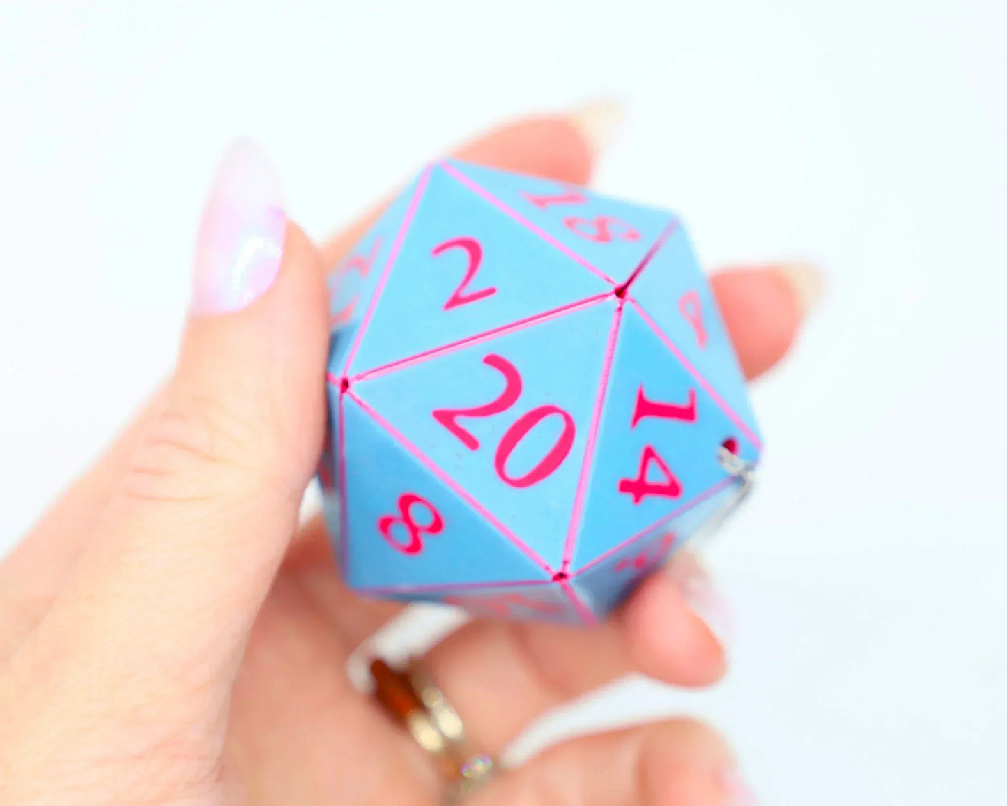 Hand holding a blue 20-sided dice with pink numbers, tabletop gaming accessory