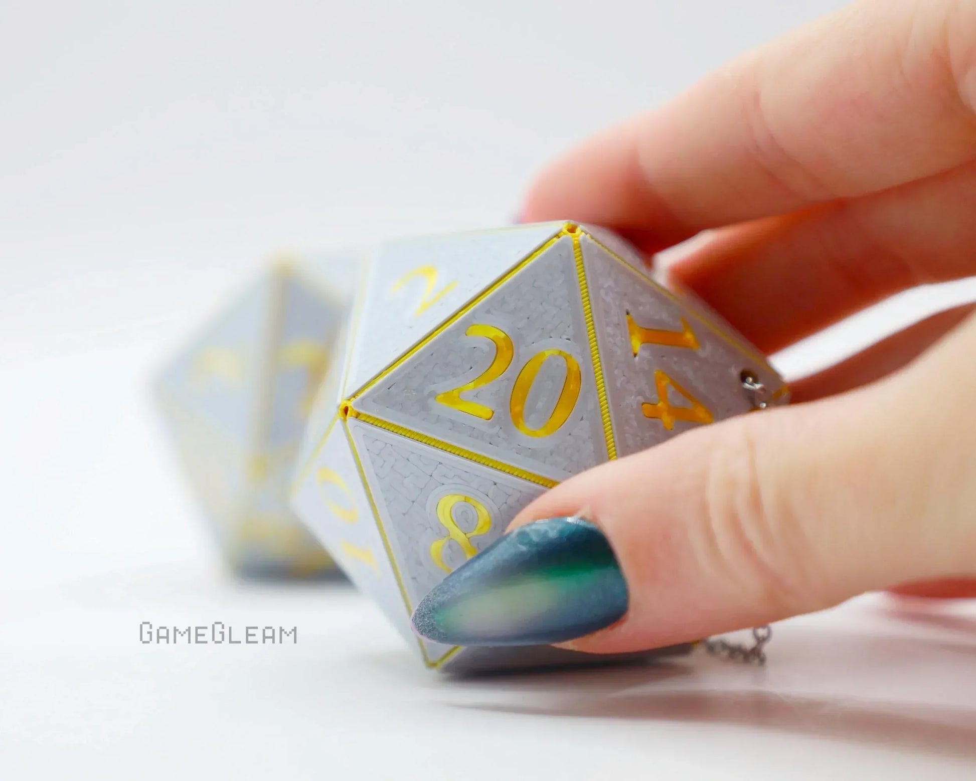Hand holding large gray and gold twenty-sided dice charm with chain on white background