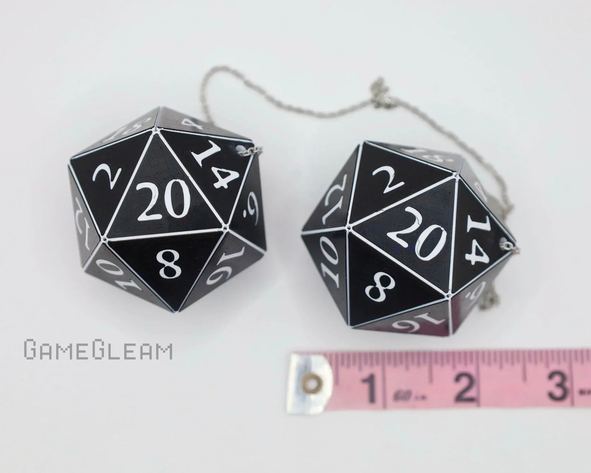 Black and white 20-sided dice car charm set with silver chain, shown next to a pink ruler for scale.