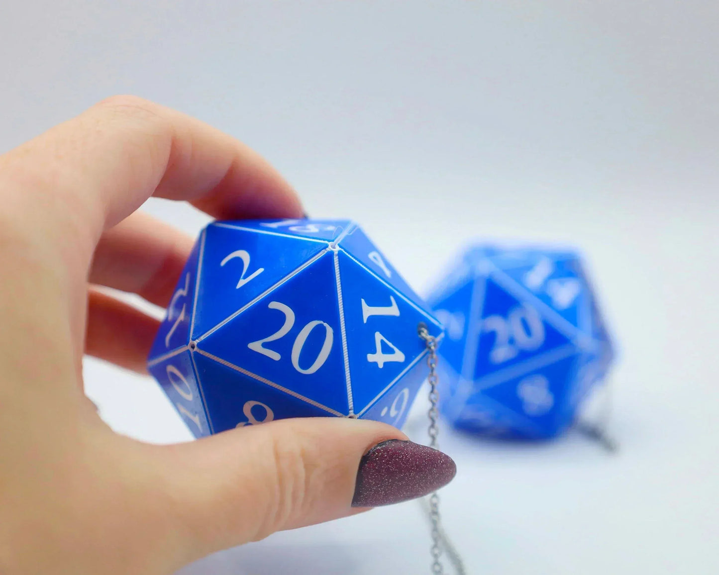 Hand holding blue 20-sided dice car charm with white numbers and metal chain