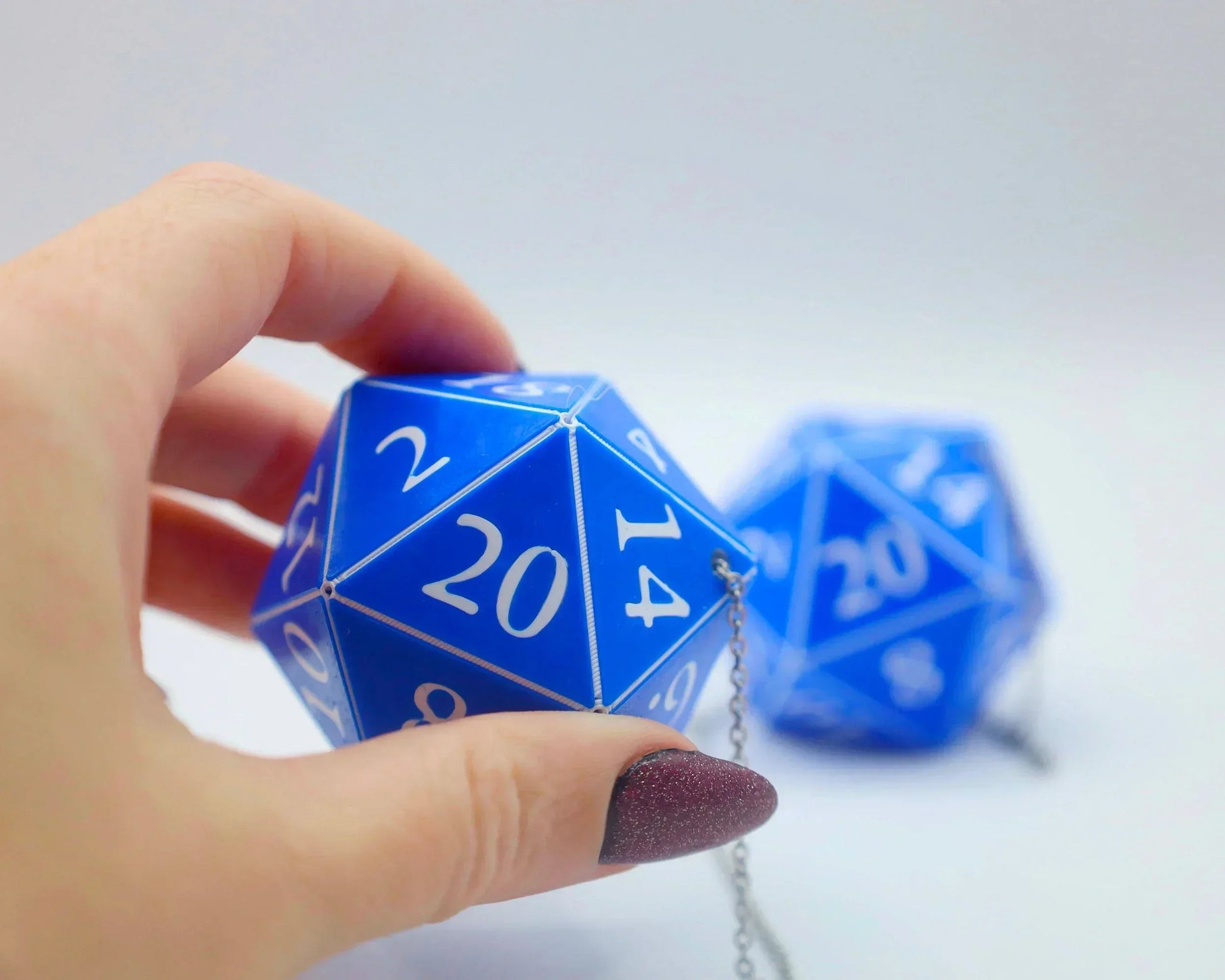 Hand holding blue 20-sided dice car charm with white numbers and metal chain