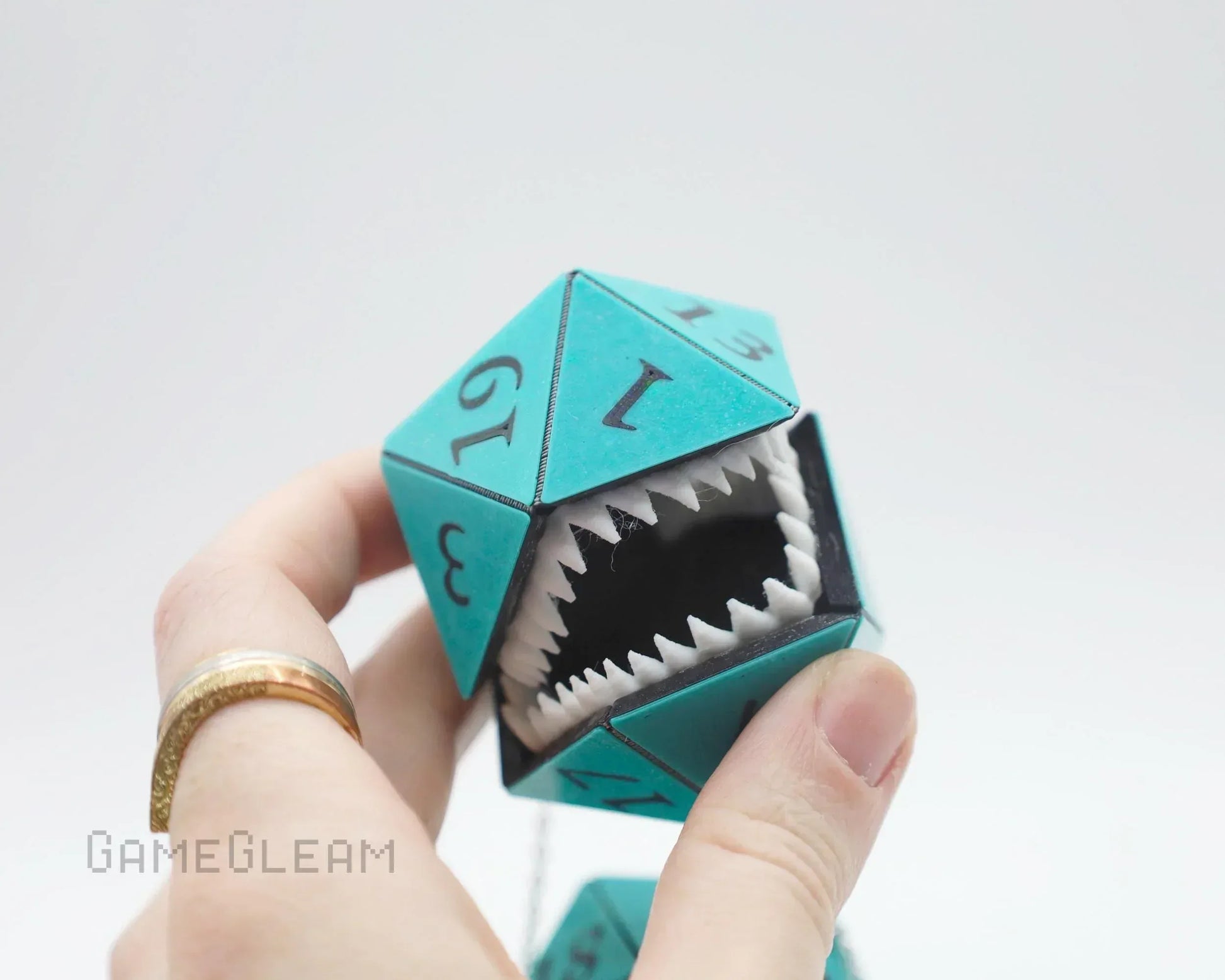 Hand holding teal twenty-sided dice charm with open jaws and sharp teeth, gamer accessory