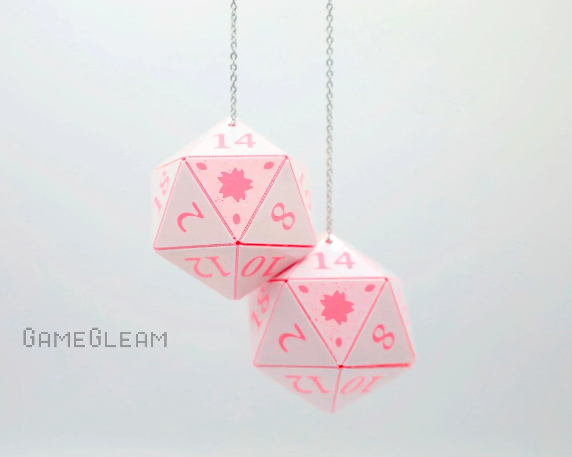 Hanging pair of pastel pink 20-sided dice charms with numbered faces on a silver chain