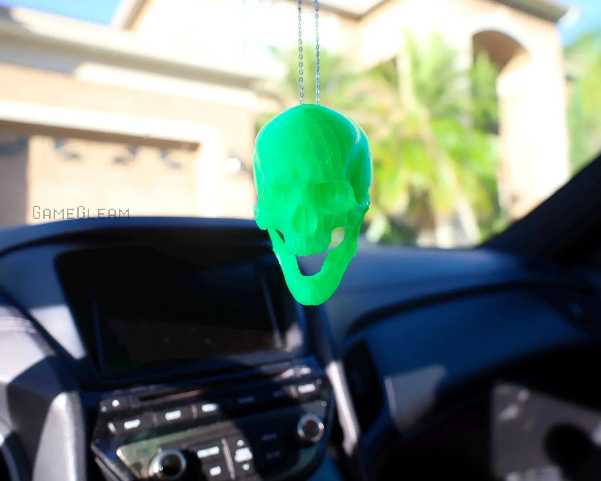 Neon green skull car charm hanging from rearview mirror in a car interior.
