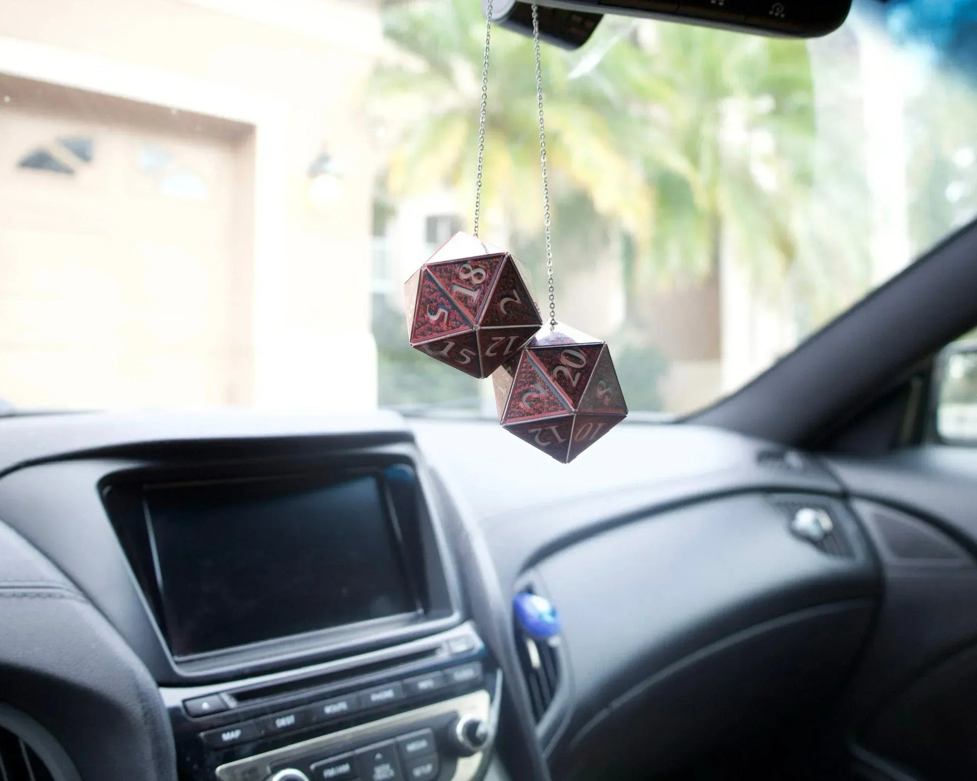 Pair of handmade red twenty-sided dice hanging as car mirror charms inside vehicle