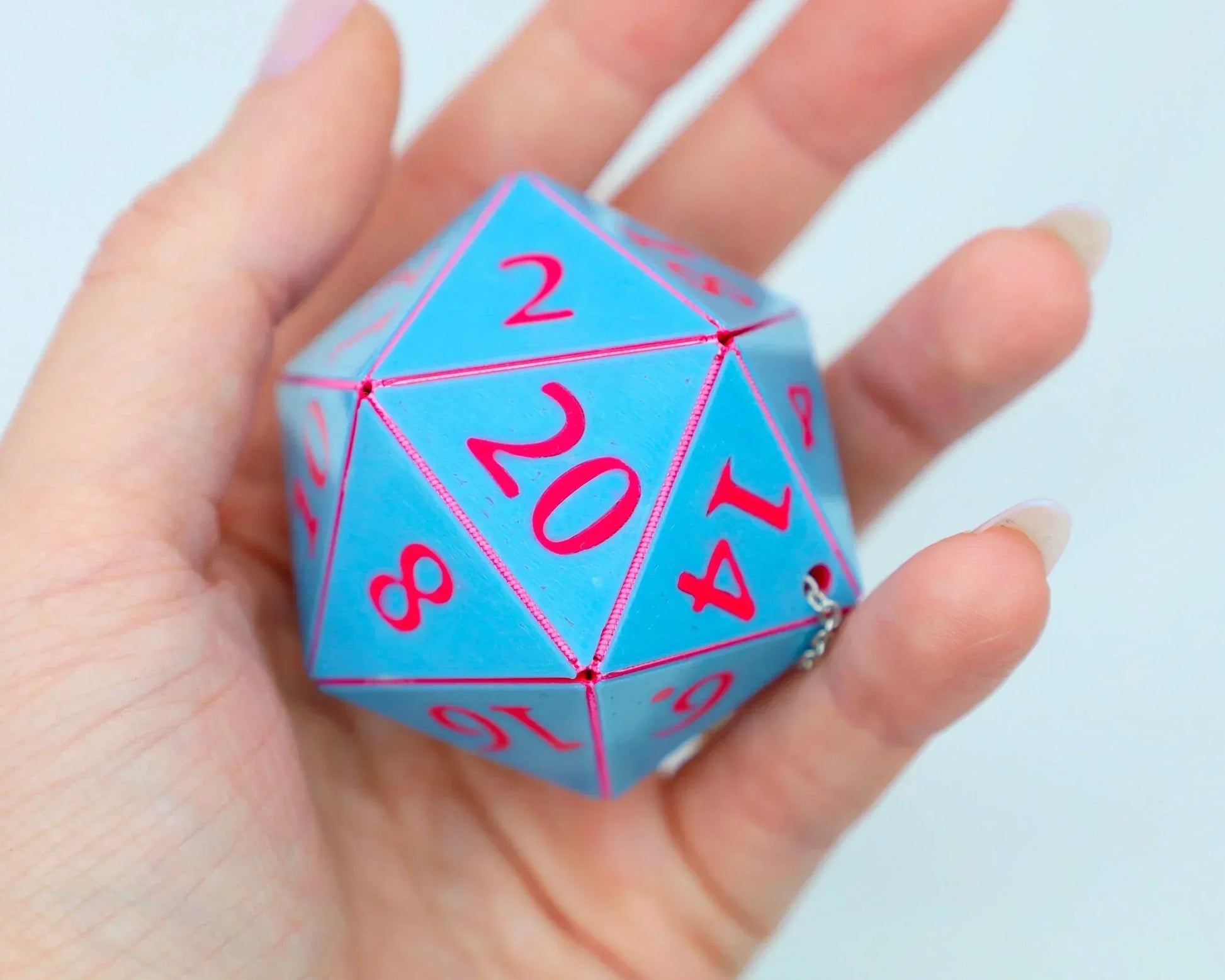 Hand holding a large blue 20-sided dice charm with pink numbers for tabletop gaming