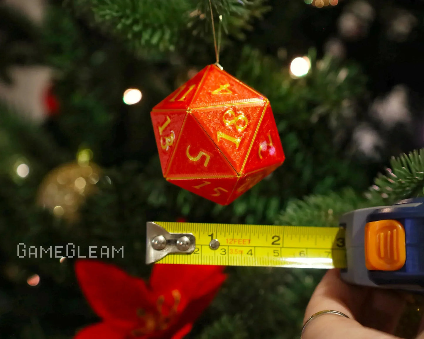 Red twenty-sided dice ornament with yellow numbers hanging on a Christmas tree, measured with tape