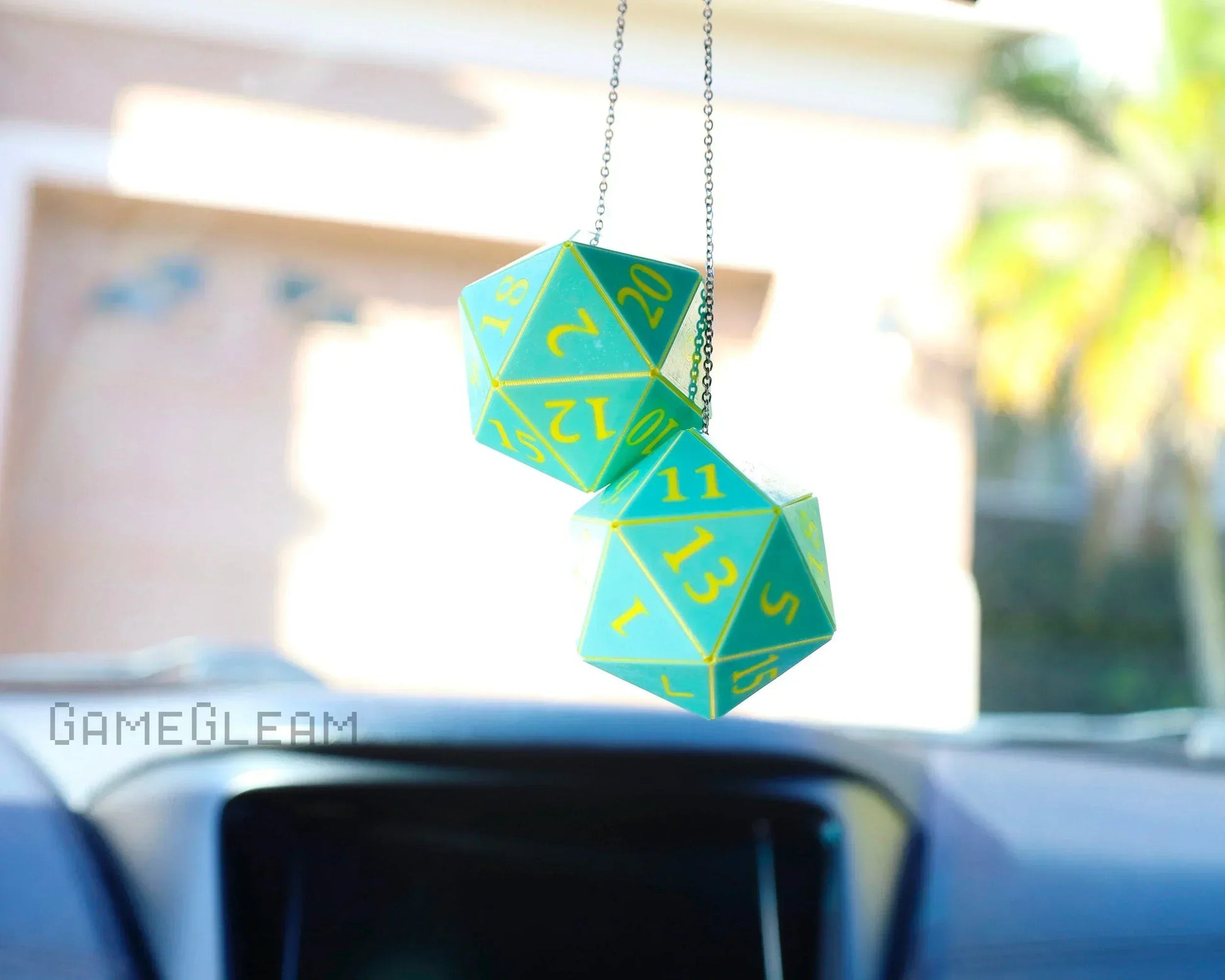 Handmade green and yellow twenty-sided dice hanging car charm accessory, sunlight in car interior.